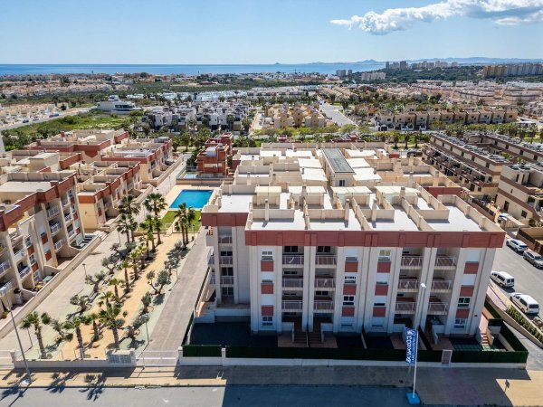 Aerial view of a 1-bed penthouse complex in Orihuela Costa with palm trees and the sea in the background.