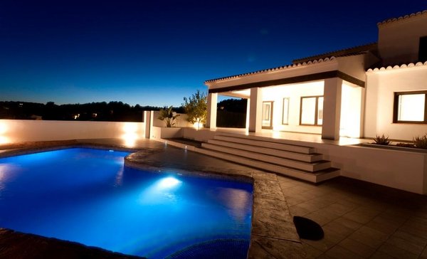Nachtfoto van het zwembadgebied van de villa met verlichte buitenkant in Moraira Teulada, Costa Blanca Noord.