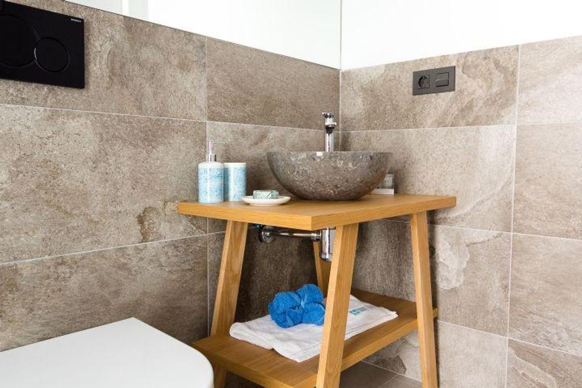 Rustieke stenen badkamerwastafel met houten standaard en blauwe accessoires in moderne Spaanse villa