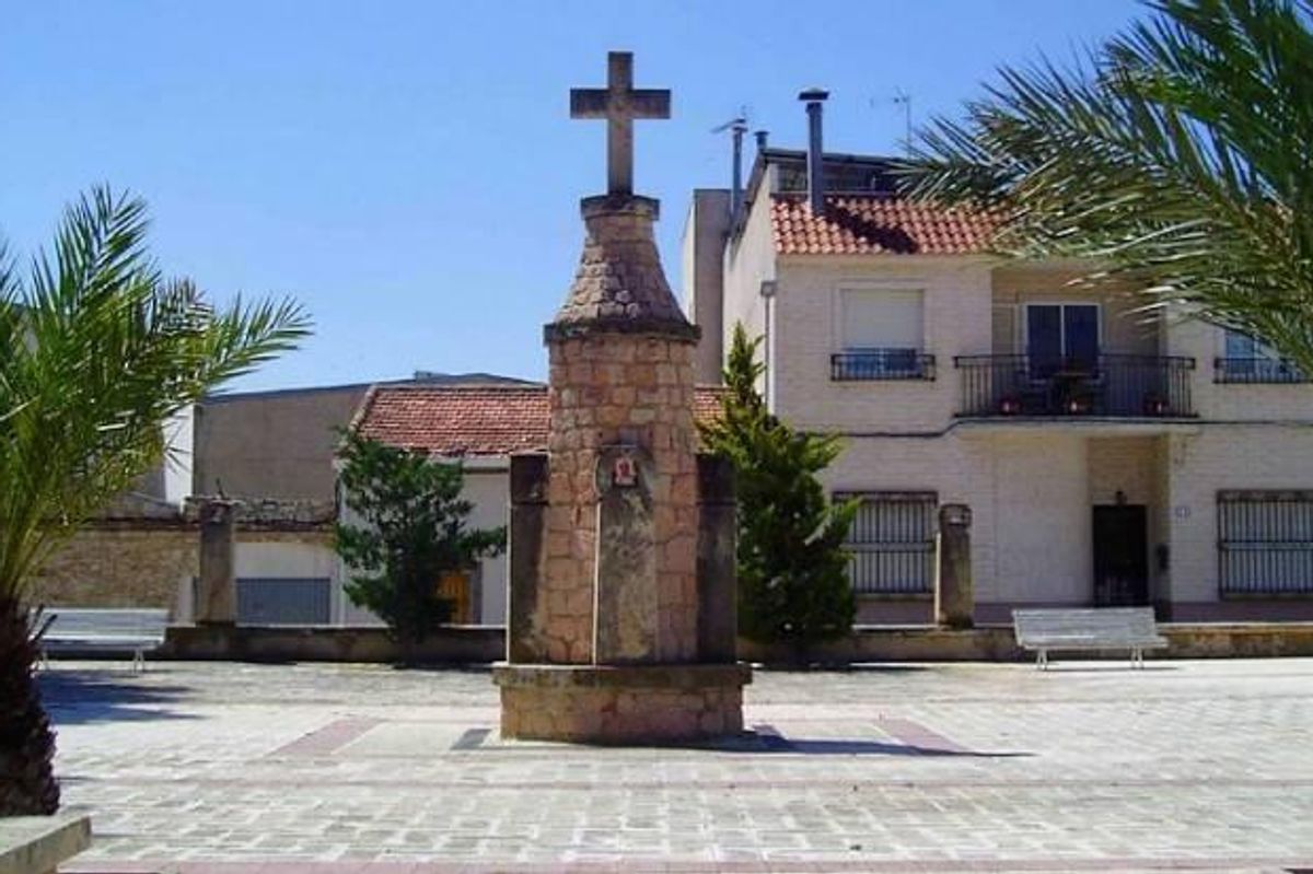 Steenen kruis monument op een plein, omringd door palmbomen in La Romana, Costa Blanca Zuid