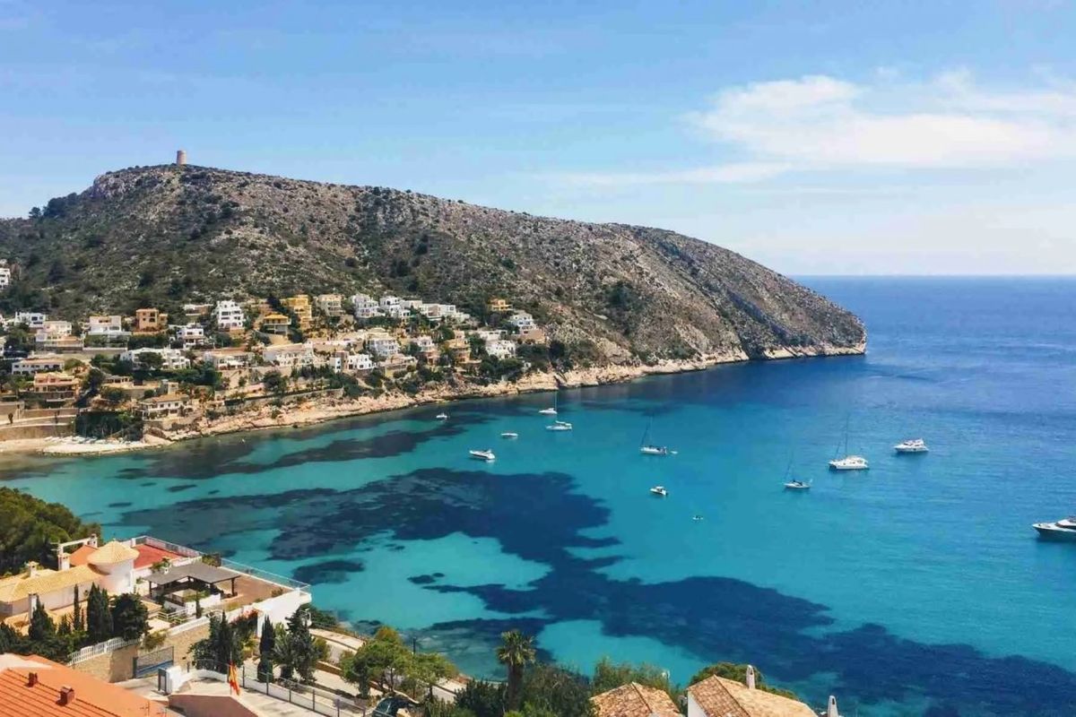 Luchtfoto van een schilderachtig strandgebied in Moraira Teulada, Costa Blanca, met helder water en groene omgeving.