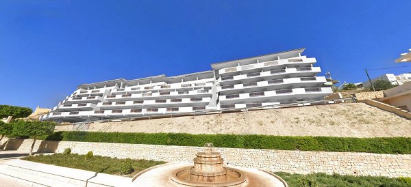 Exterior of a multi-story white apartment building with terraces in Relleu, Costa Blanca North, set on a hillside with landscaped gardens.