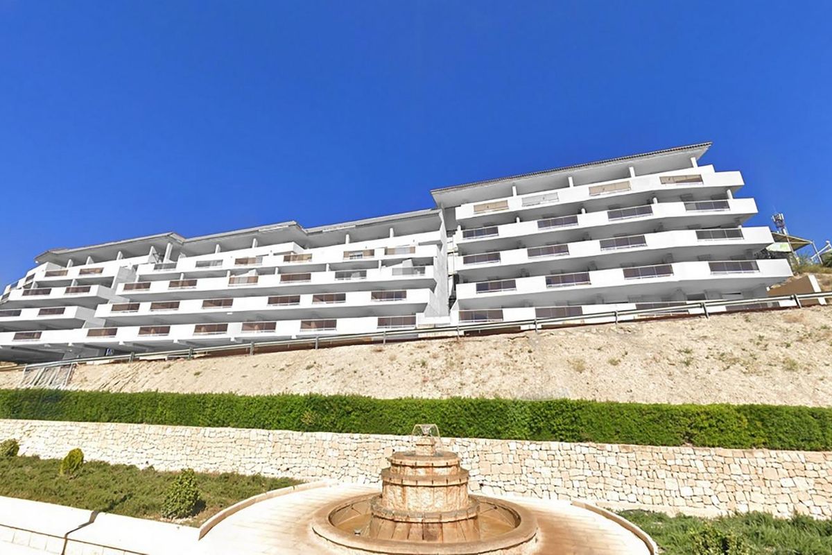 Exterior of a multi-story white apartment building with terraces in Relleu, Costa Blanca North, set on a hillside with landscaped gardens.