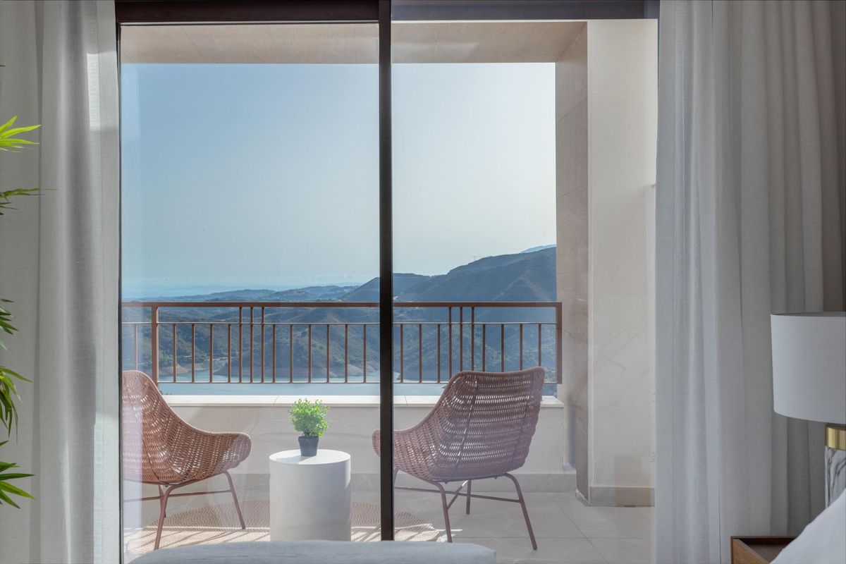 Heldere slaapkamer met uitzicht op twee stoelen en bergen buiten het raam in Istán, Costa del Sol.