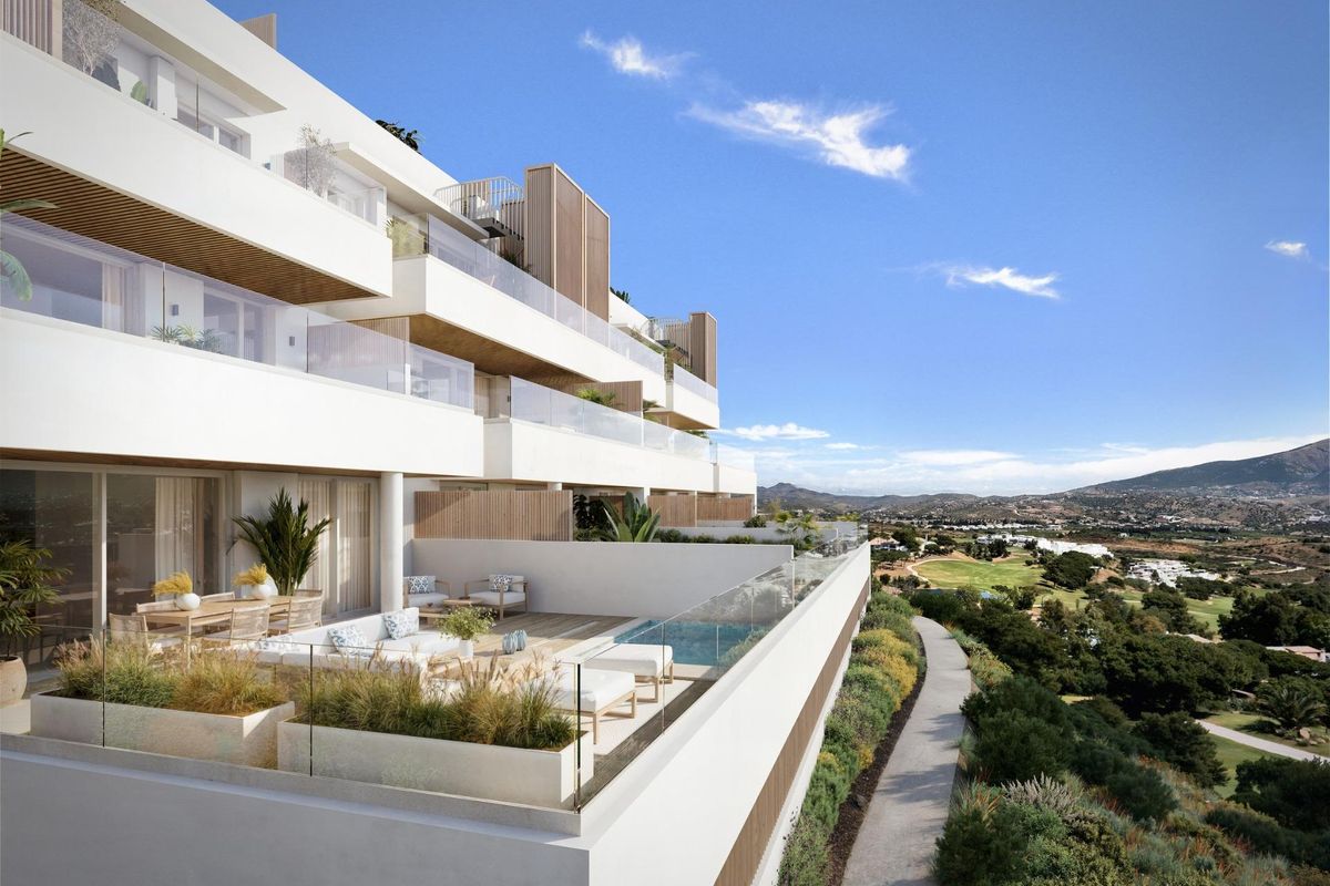 Moderne witte appartementsgebouw met glazen balkons met uitzicht op een golfbaan en bergen in Mijas