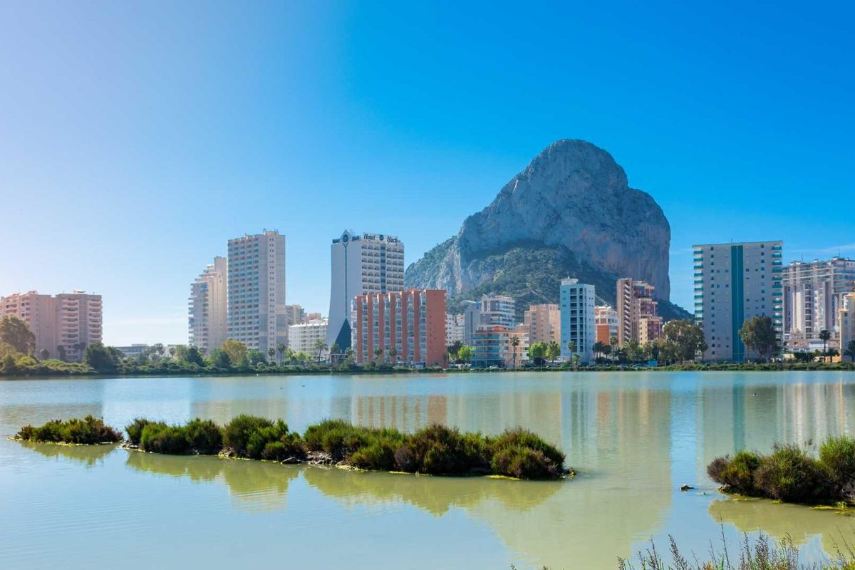 Uitzicht op Calpe met hoge gebouwen en rotsformatie bij een rustige vijver in Costa Blanca Noord.