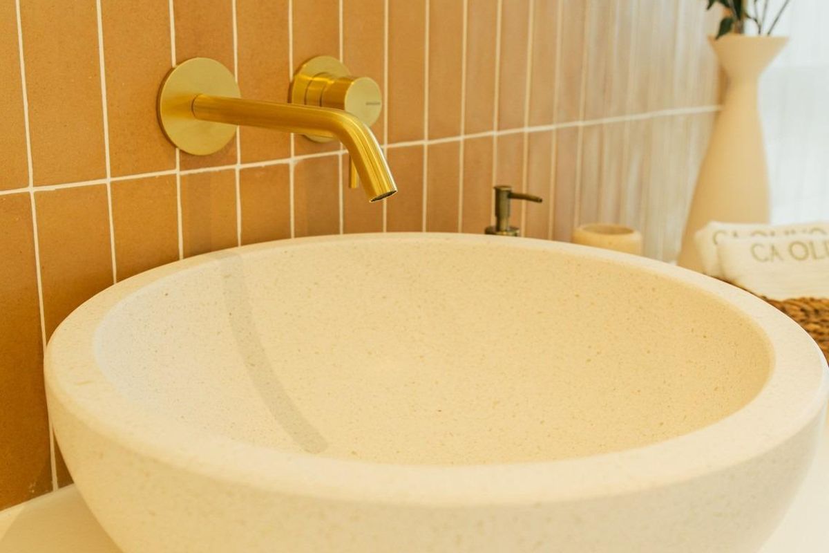 Close-up van een unieke stenen wastafel en gouden armaturen in een moderne badkamer van een villa in Jávea Xàbia.