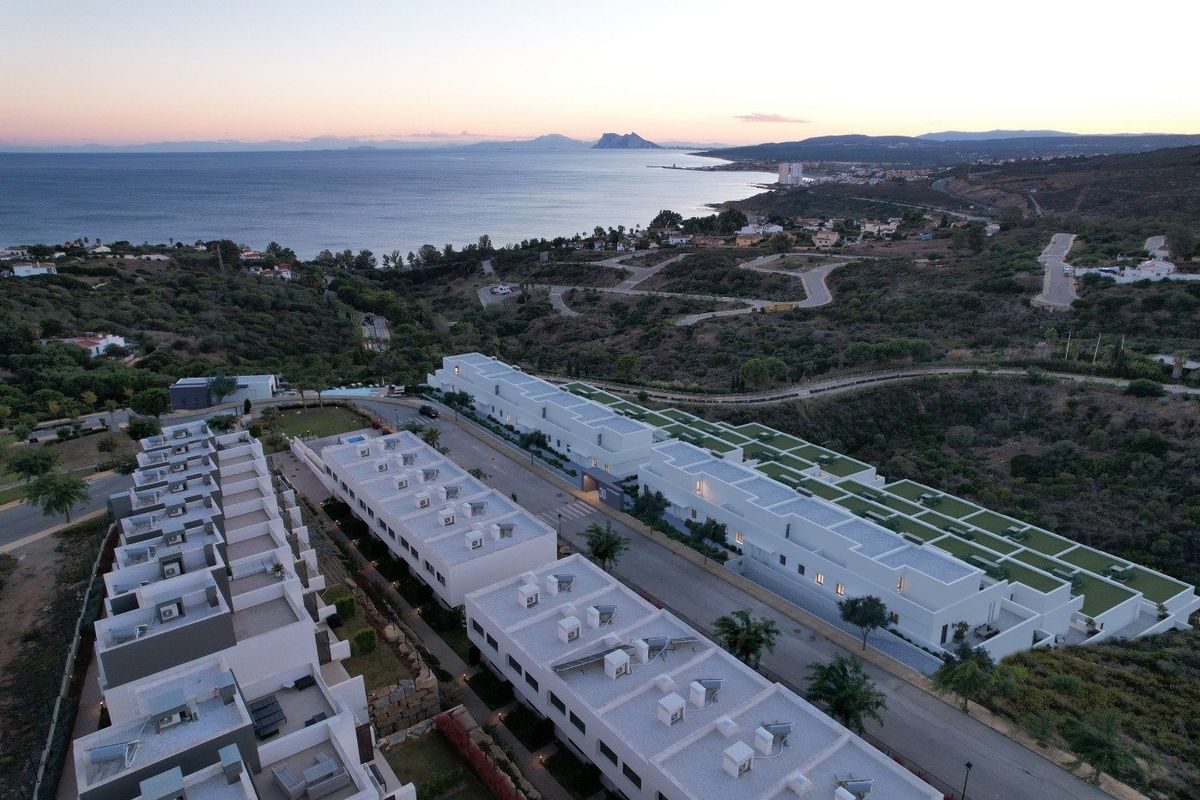 Aerial view of white townhouses in Manilva, Costa del Sol, Spain. Ocean and distant mountains in background. Modern, low-rise properties.