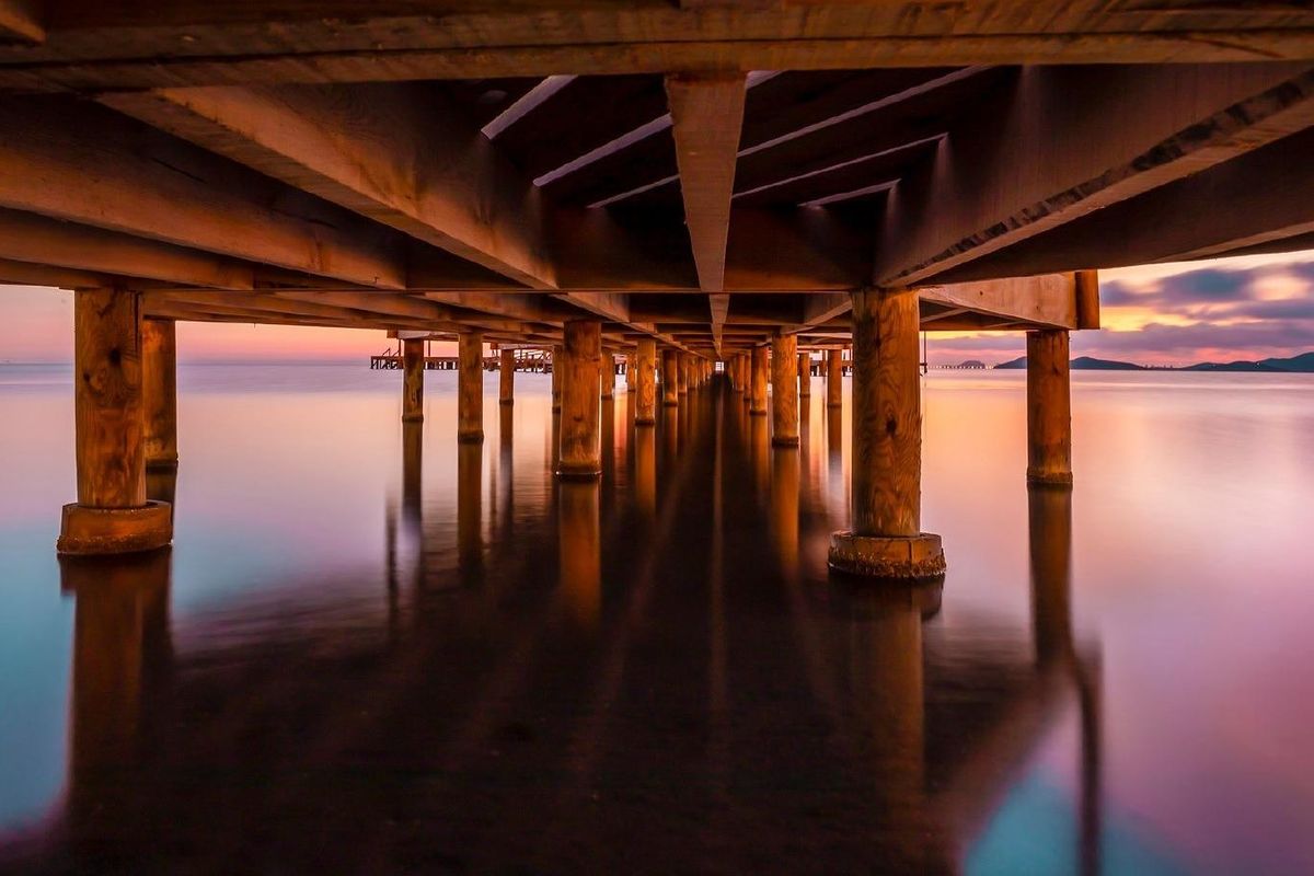 Onder een houten pier bij zonsondergang, met een rustig water nabij La Manga del Mar Menor.