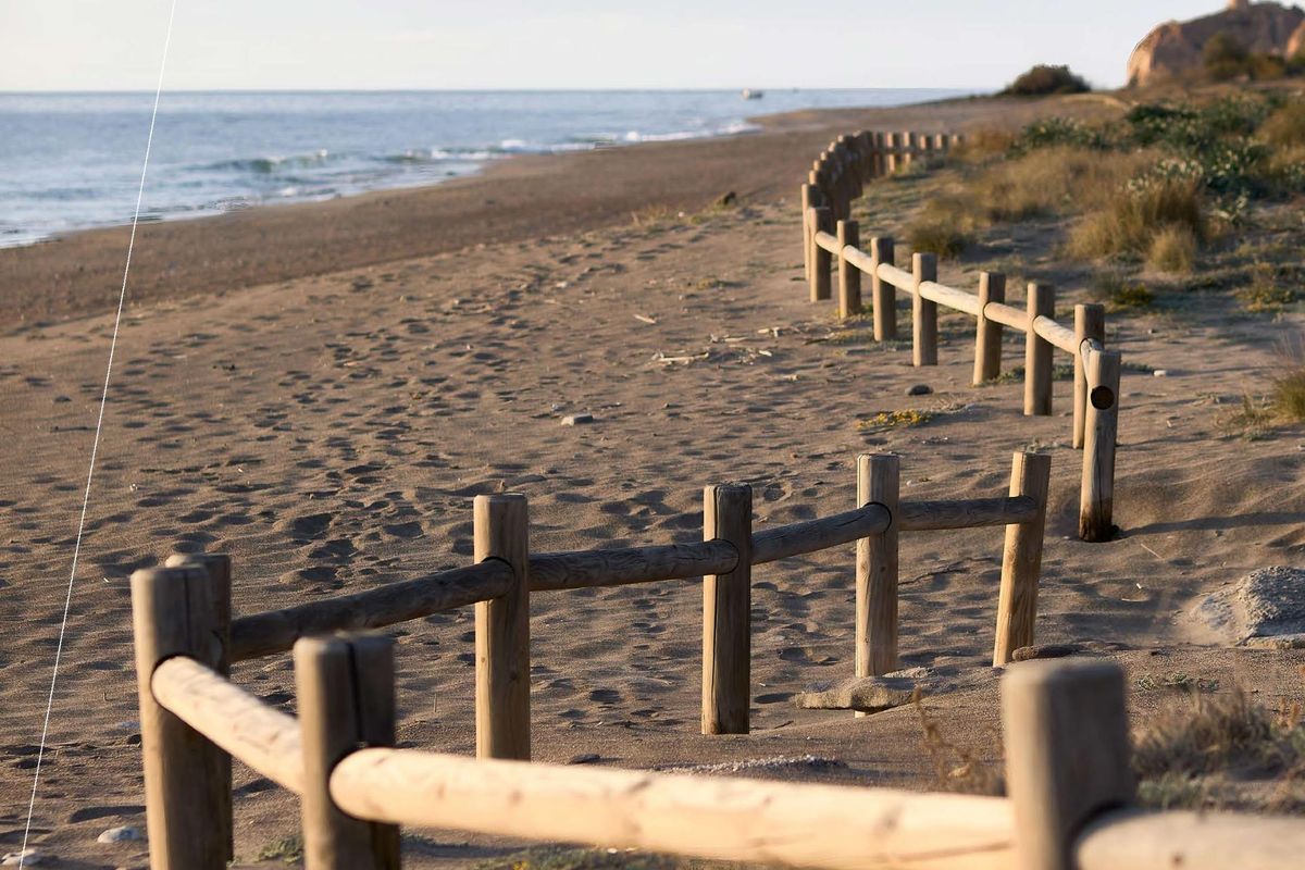 Rustiek strandzicht in Mojacar met houten omheining en zachte golven, ideaal voor ontspanning.