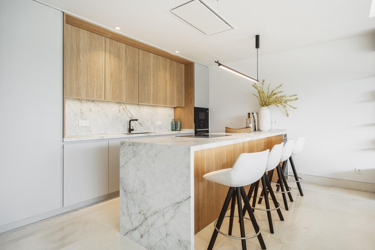 Moderne keuken in een appartement in Marbella met marmeren werkbladen en stijlvolle barstoelen voor drie.