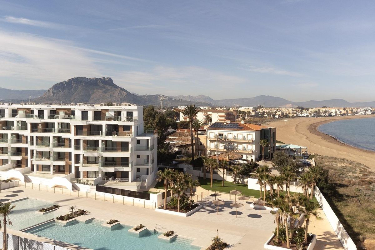 Luchtbeeld van een modern appartementencomplex nabij het strand in Denia, met bergen op de achtergrond.