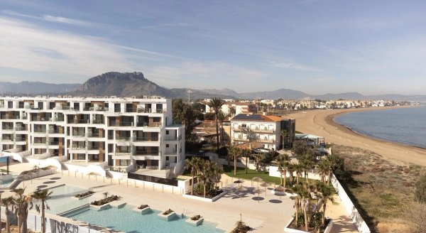 Luchtbeeld van een modern appartementencomplex nabij het strand in Denia, met bergen op de achtergrond.