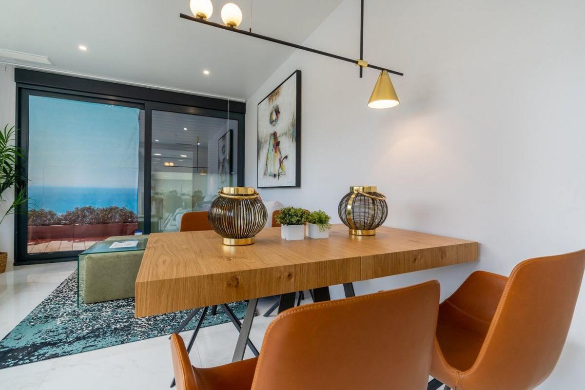 Eetruimte met een houten tafel onder hanglampen, met uitzicht op de oceaan in een appartement in Benidorm.