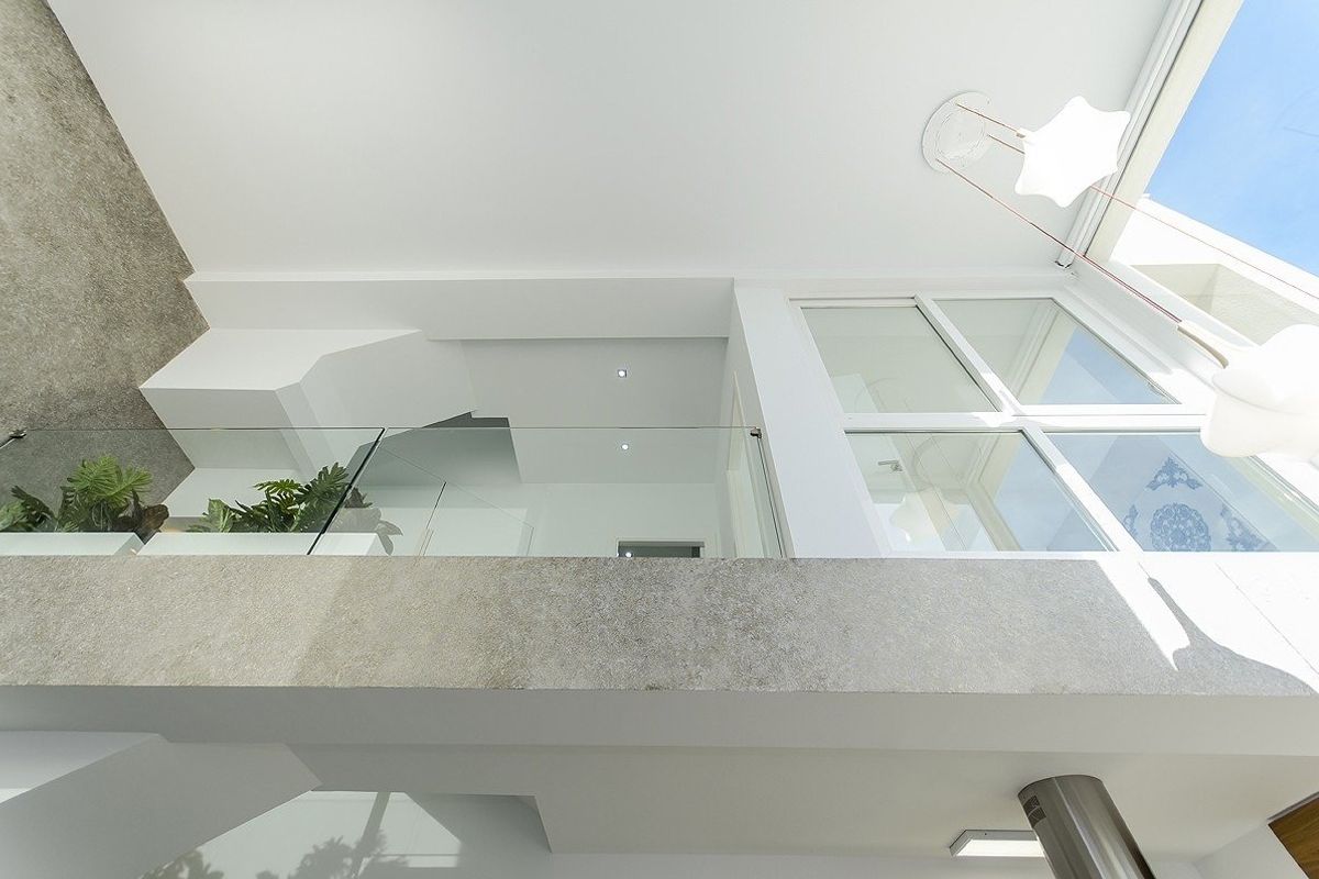 Opwaartse blik op een moderne trap in de villa, met glazen leuningen en natuurlijk licht van boven.