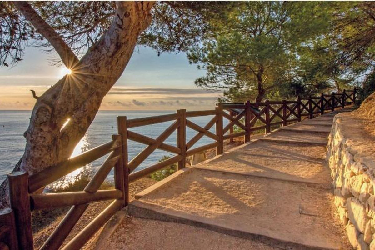 In de zon verlicht pad langs de kust in Benissa, Costa Blanca Noord, omringd door bomen en met uitzicht op zee.