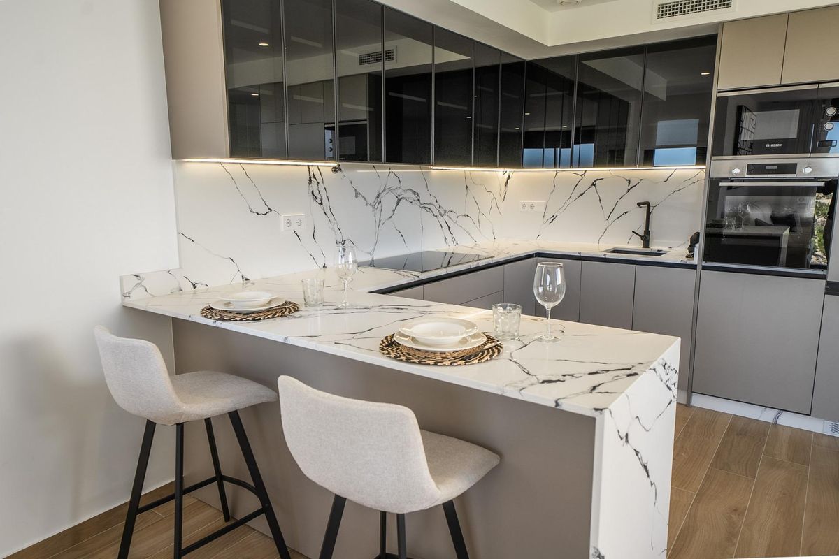 Moderne keuken met strakke kasten, marmeren aanrechten en barkrukken in een villa in Algorfa, Spanje.