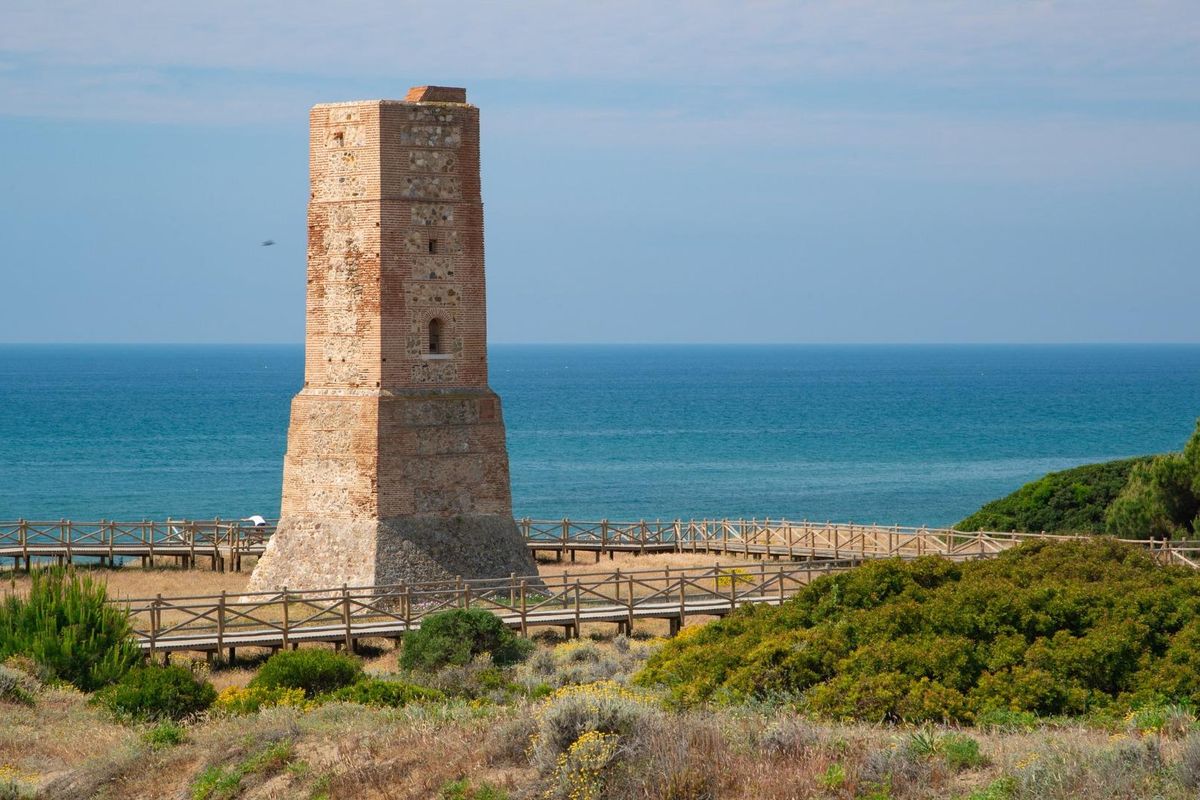 Historische toren met uitzicht op de zee in Marbella, Costa del Sol, omringd door kustvegetatie.