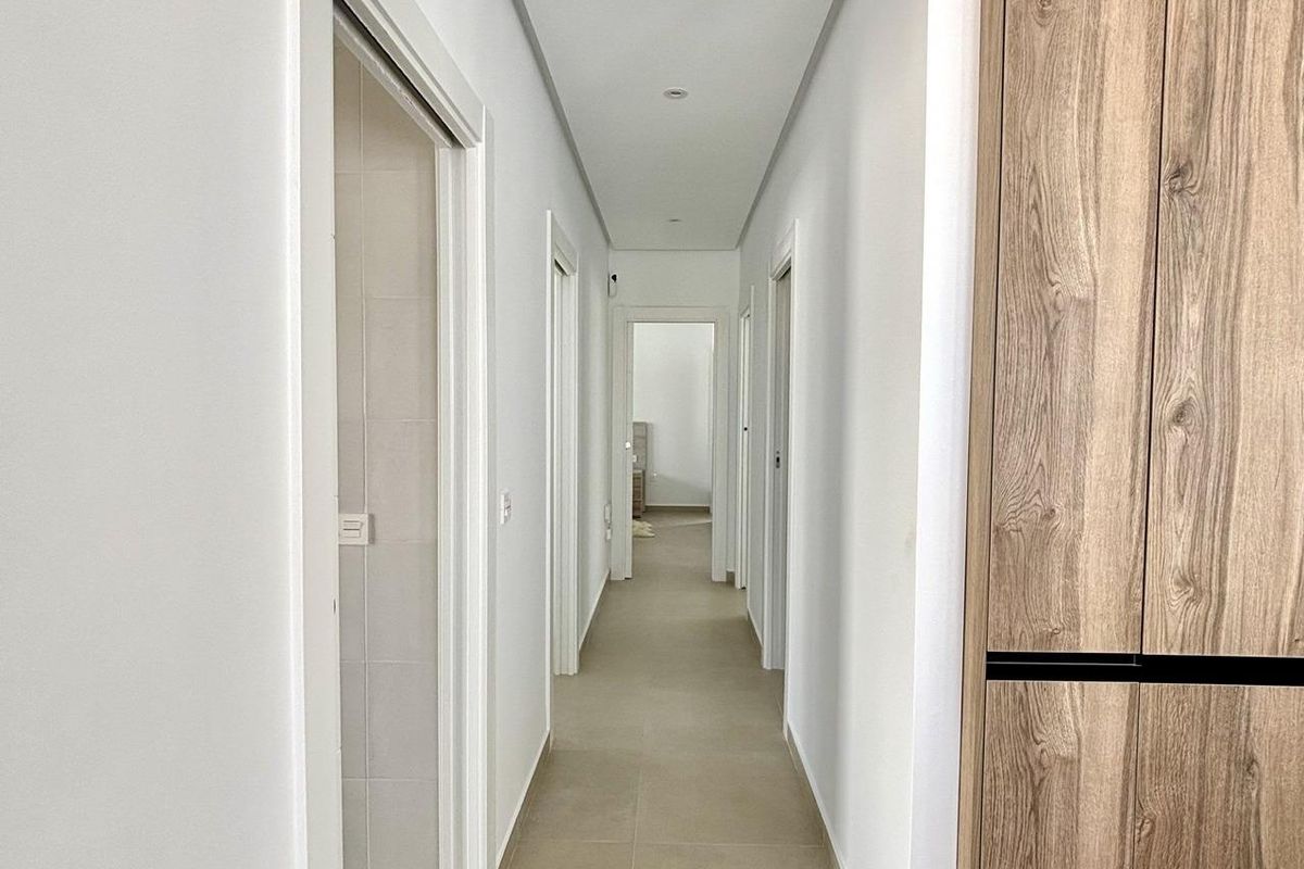 Lange gang met witte muren die naar verschillende kamers leidt in een moderne villa in Benijofar.