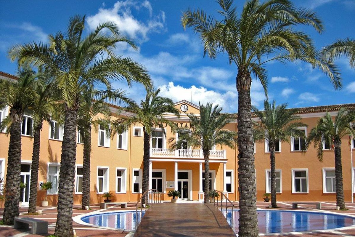 Grootse entree van een luxe gebouw in Costa Blanca, omringd door palmbomen en waterpartijen.