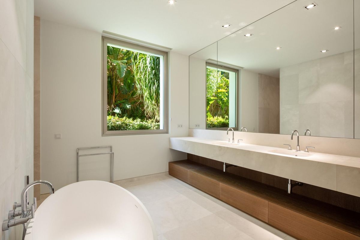 Moderne badkamer in een villa in Casares met dubbele wastafels en weelderige planten buiten het raam.