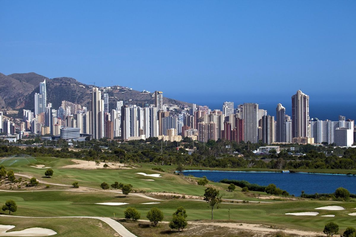 Panoramisch uitzicht op een golfbaan in Benidorm, met de skyline van de stad en bergen op de achtergrond.