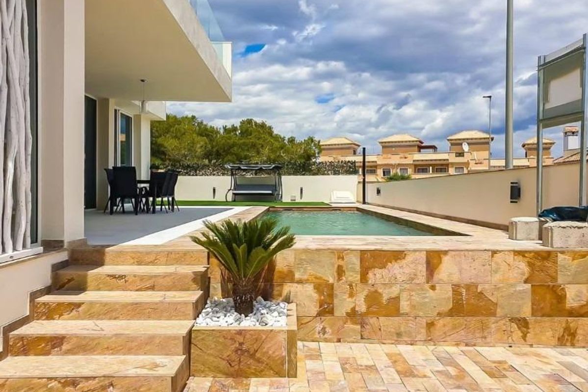 Private terrace area with pool at a three-bedroom villa in Orihuela Costa, surrounded by lush greenery.