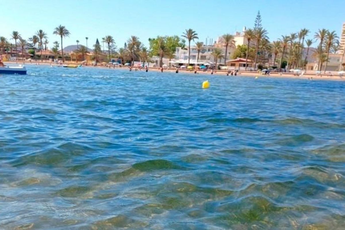 Helder water op een strand in Costa Calida, waar bezoekers genieten van de zon en zwemmen onder een heldere lucht.