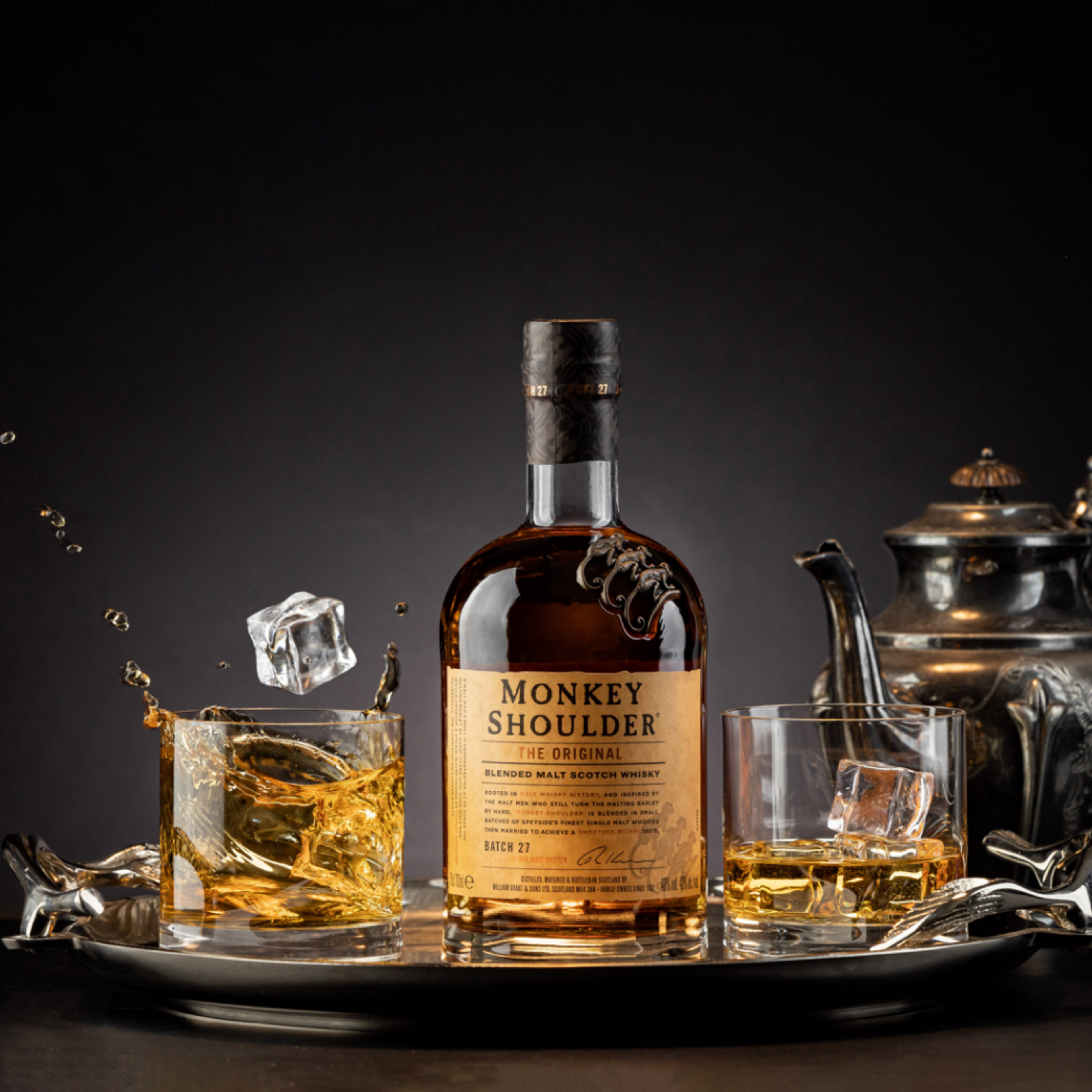Monkey Shoulder whisky bottle with splashing glasses on a silver tray, dark drinks photography