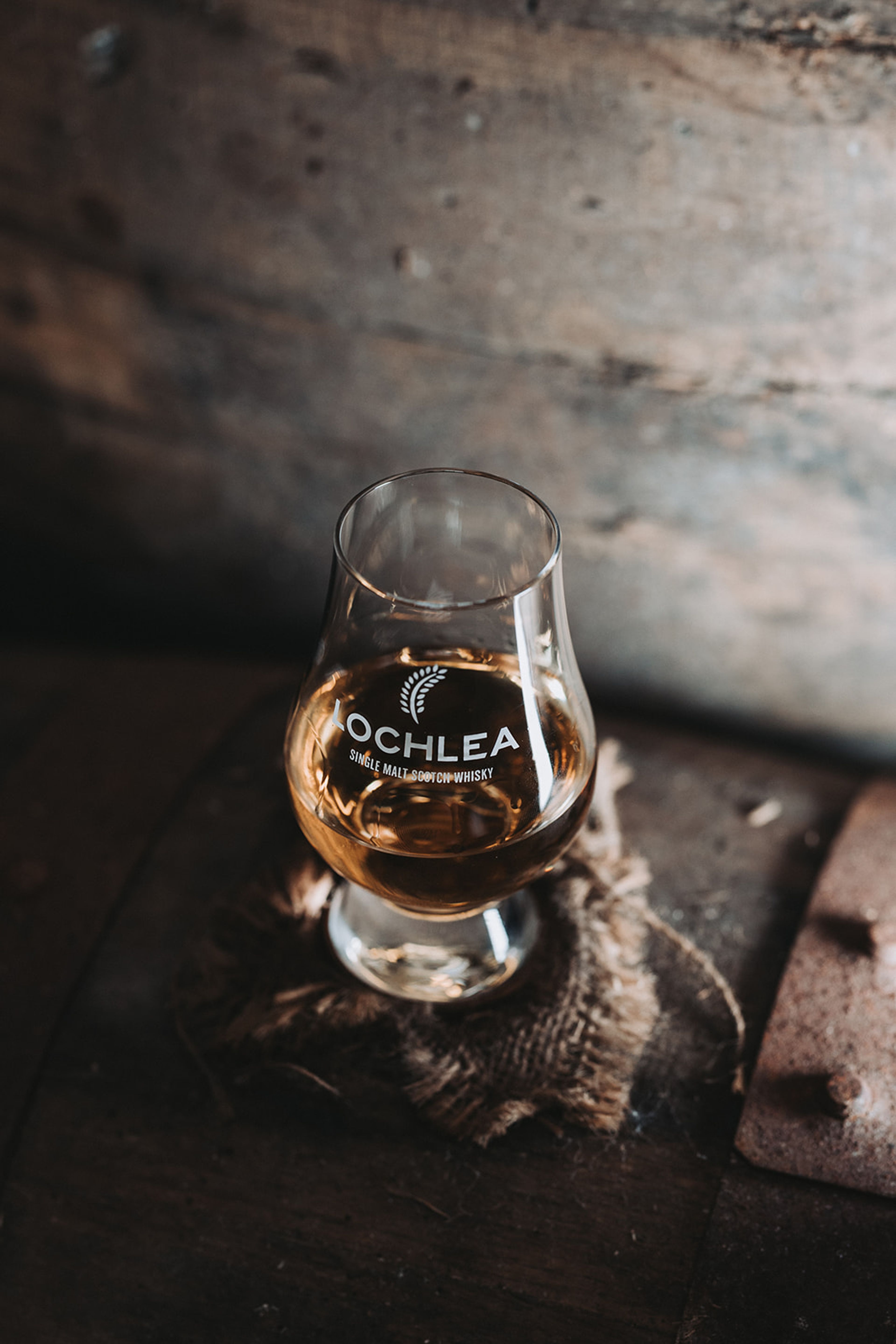 Glass of Lochlea single malt whisky on hessian atop a wooden cask