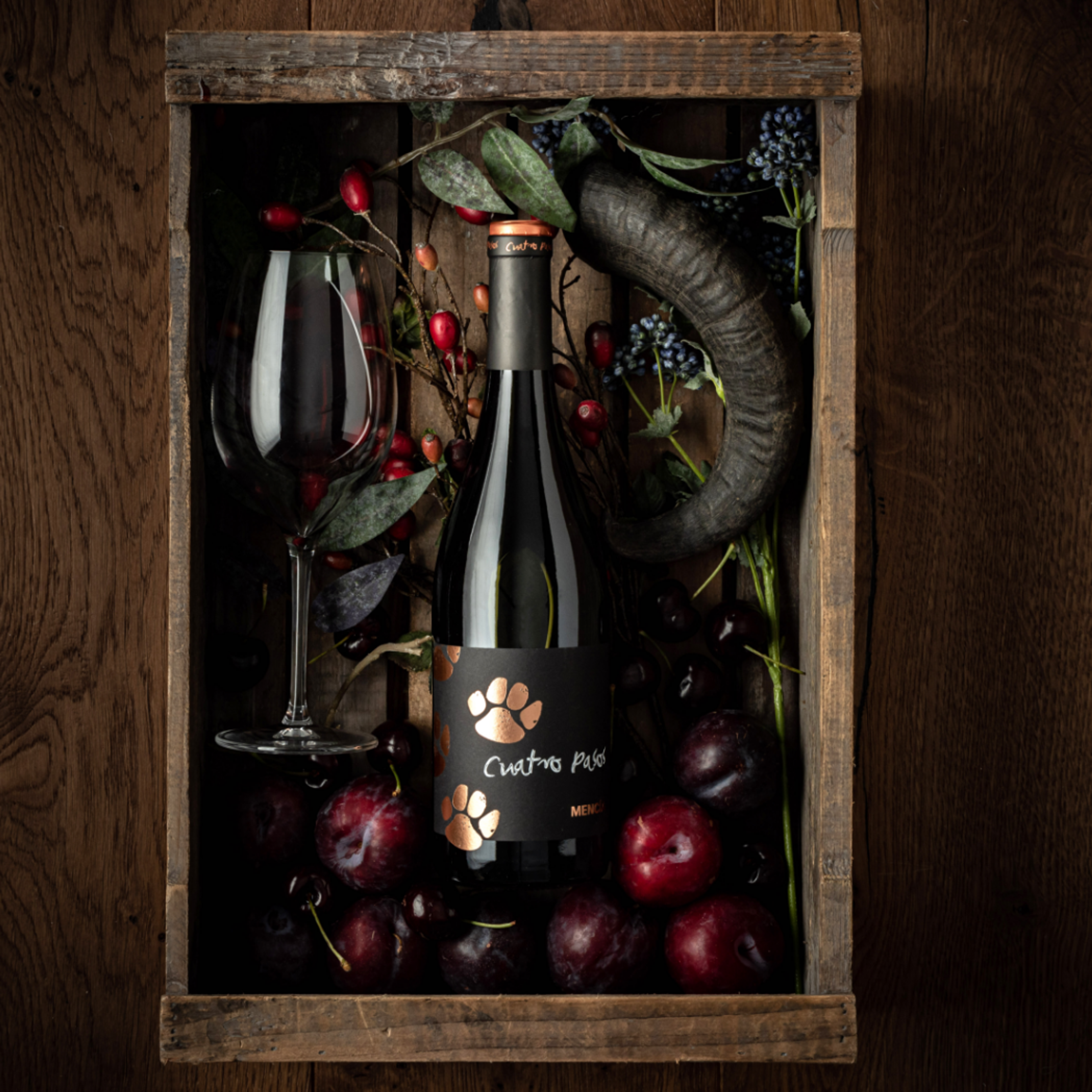 Cuatro Pasos wine bottle styled in a rustic wooden crate with plums, cherries and foliage