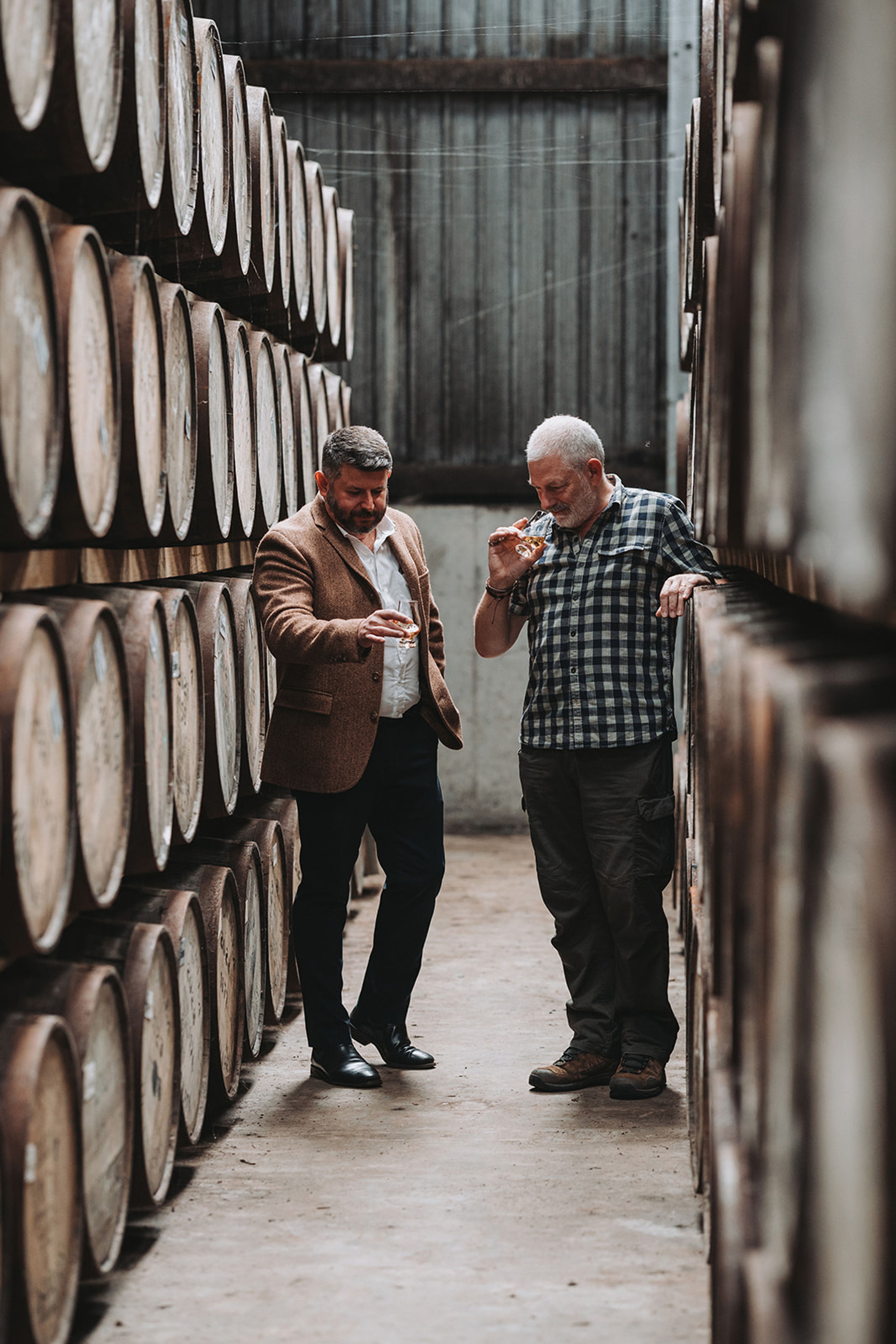Two men nosing whisky between racks of casks in the Lochlea distillery warehouse