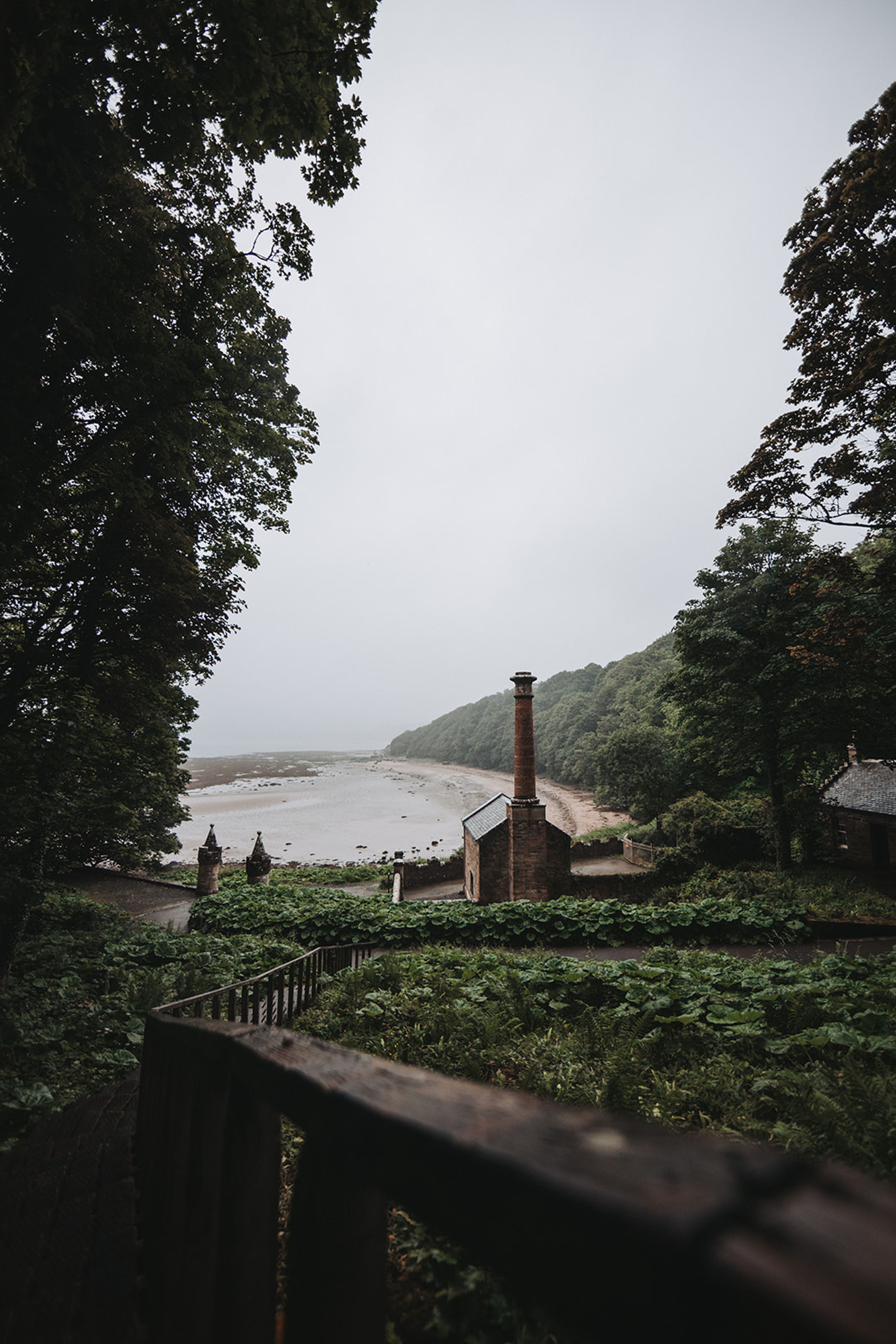 Stone building with a tall brick chimney overlooking a misty beach cove on the Scottish coast
