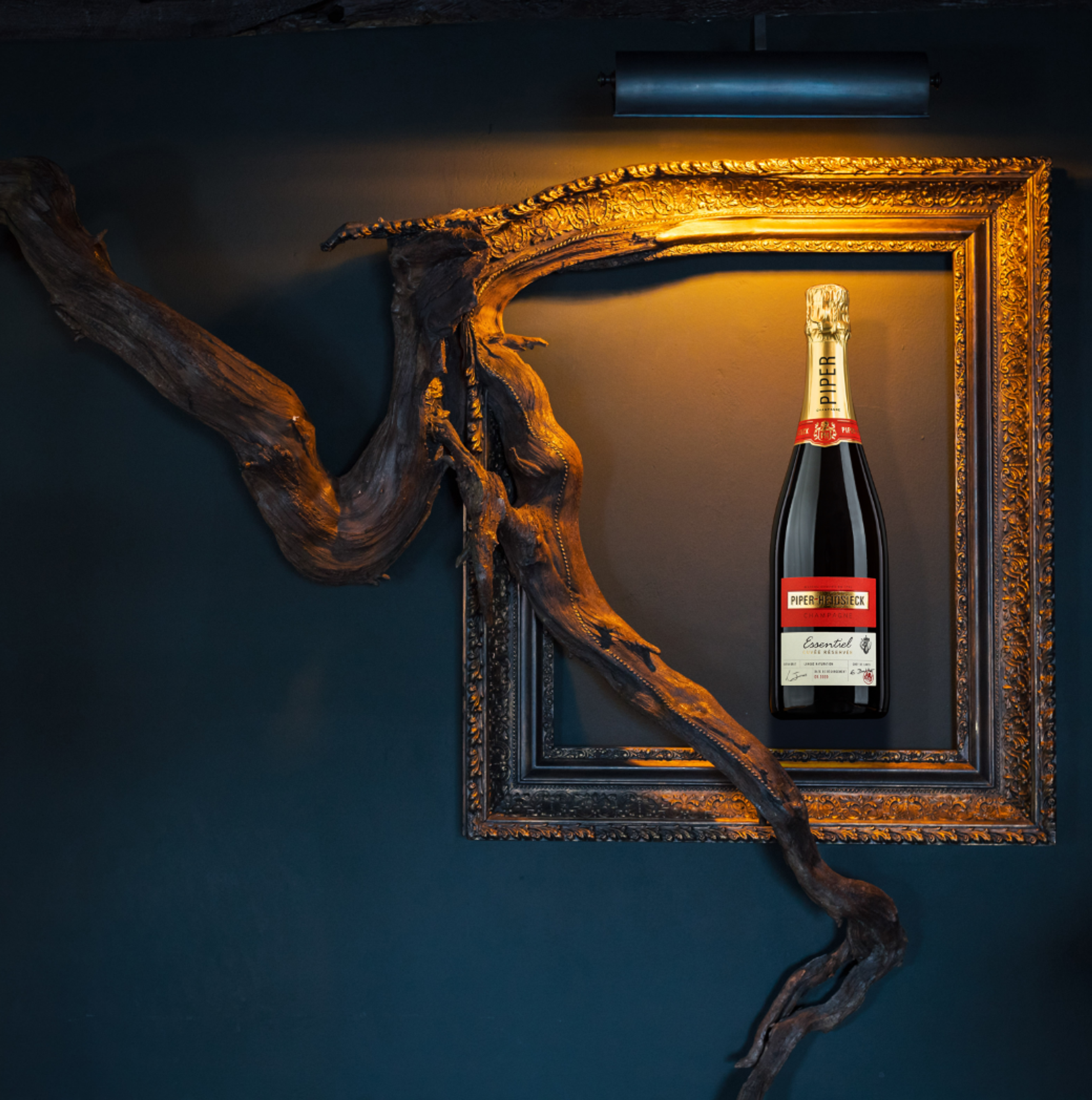 Piper-Heidsieck champagne bottle spotlit in an ornate gilded frame entwined with driftwood