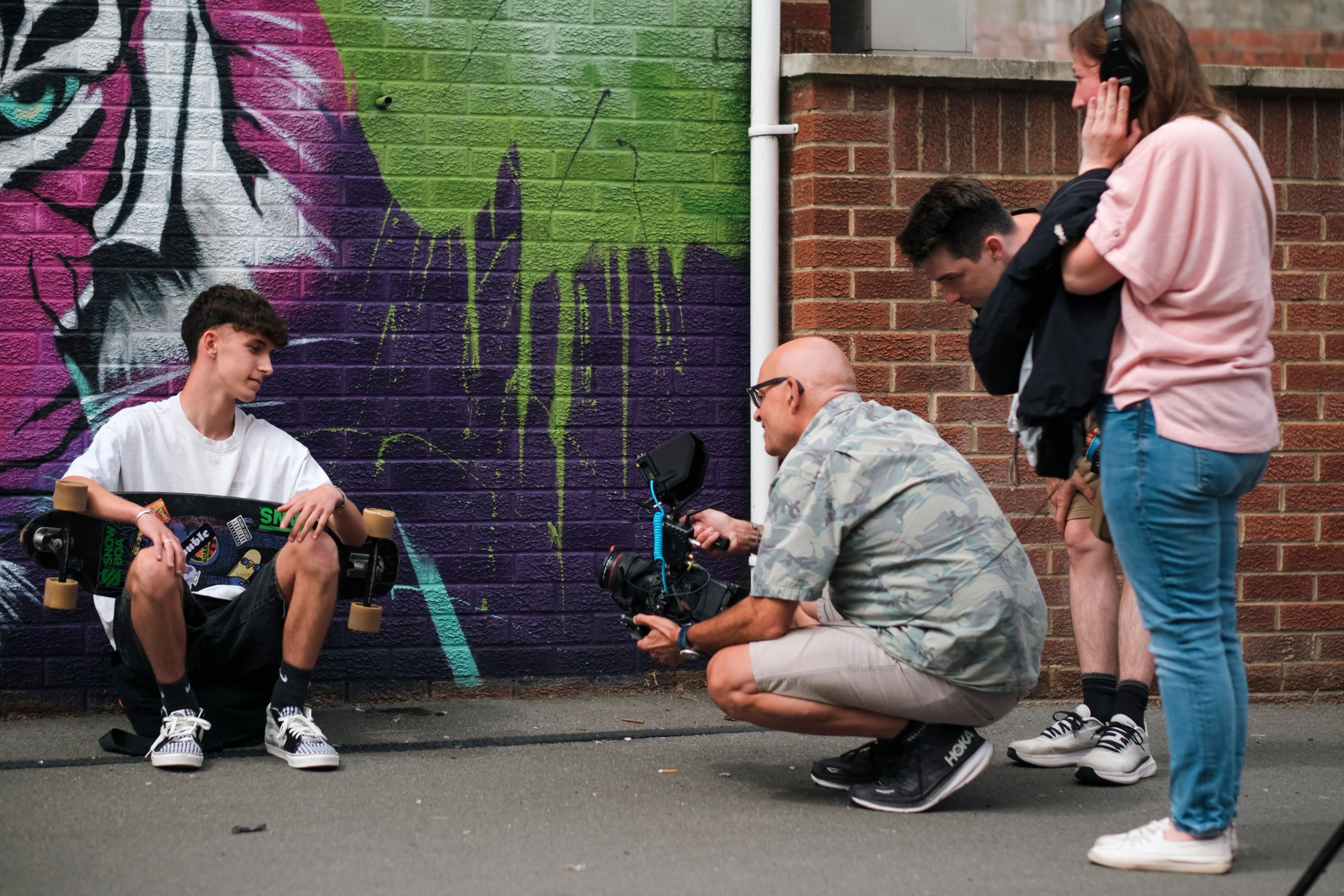 Film crew crouching to shoot a young skateboarder against a graffiti wall for BeU Swindon