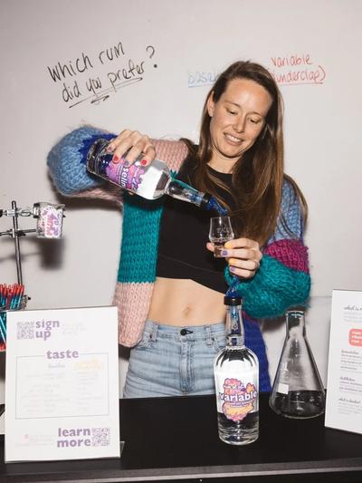 Robyn Smith of rum et al. pouring a measure into a tasting glass beside a whiteboard asking “Which rum did you prefer?”