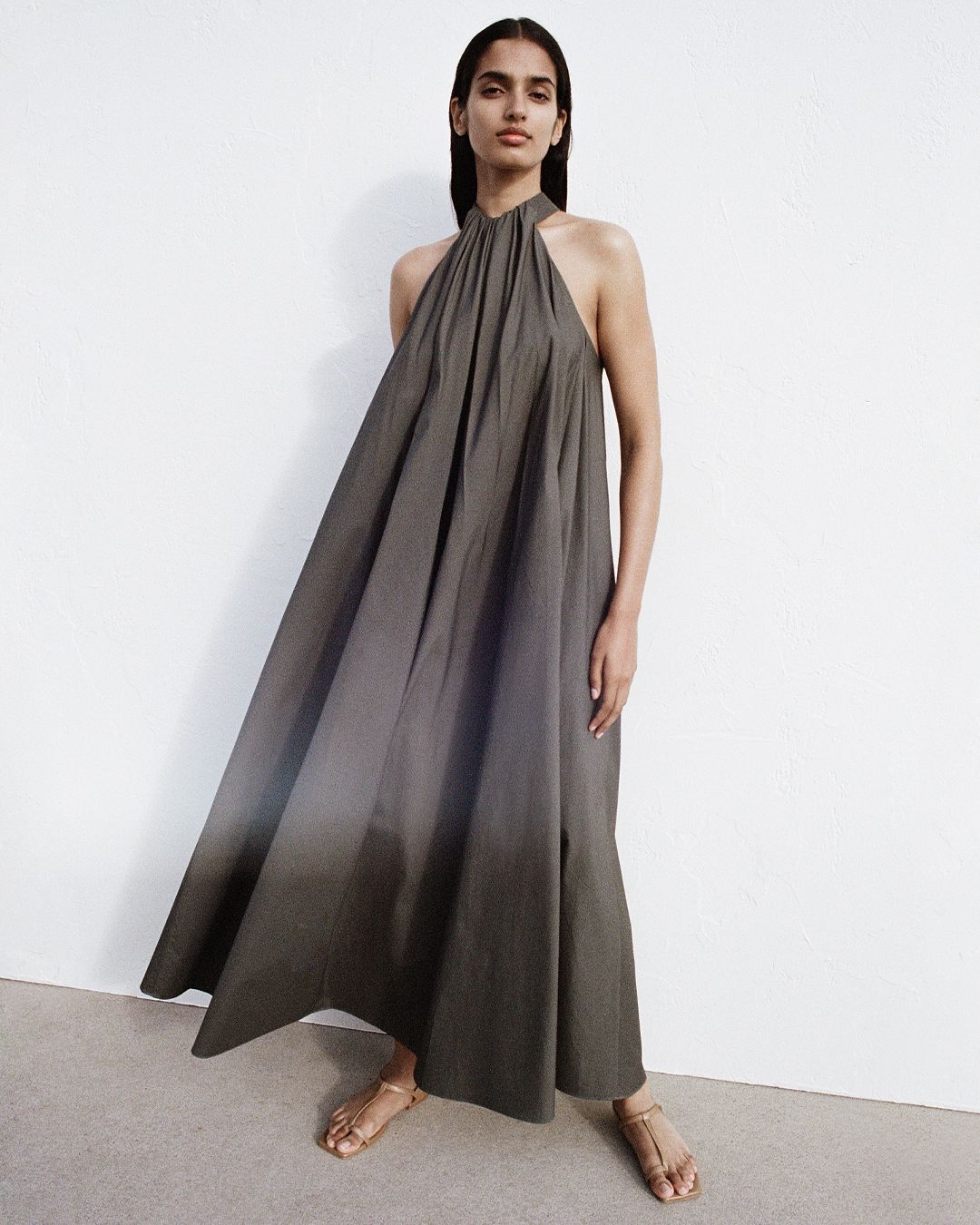 Girl in dark green dress with high neck, with wind blowing through her dress showing pleat detail.