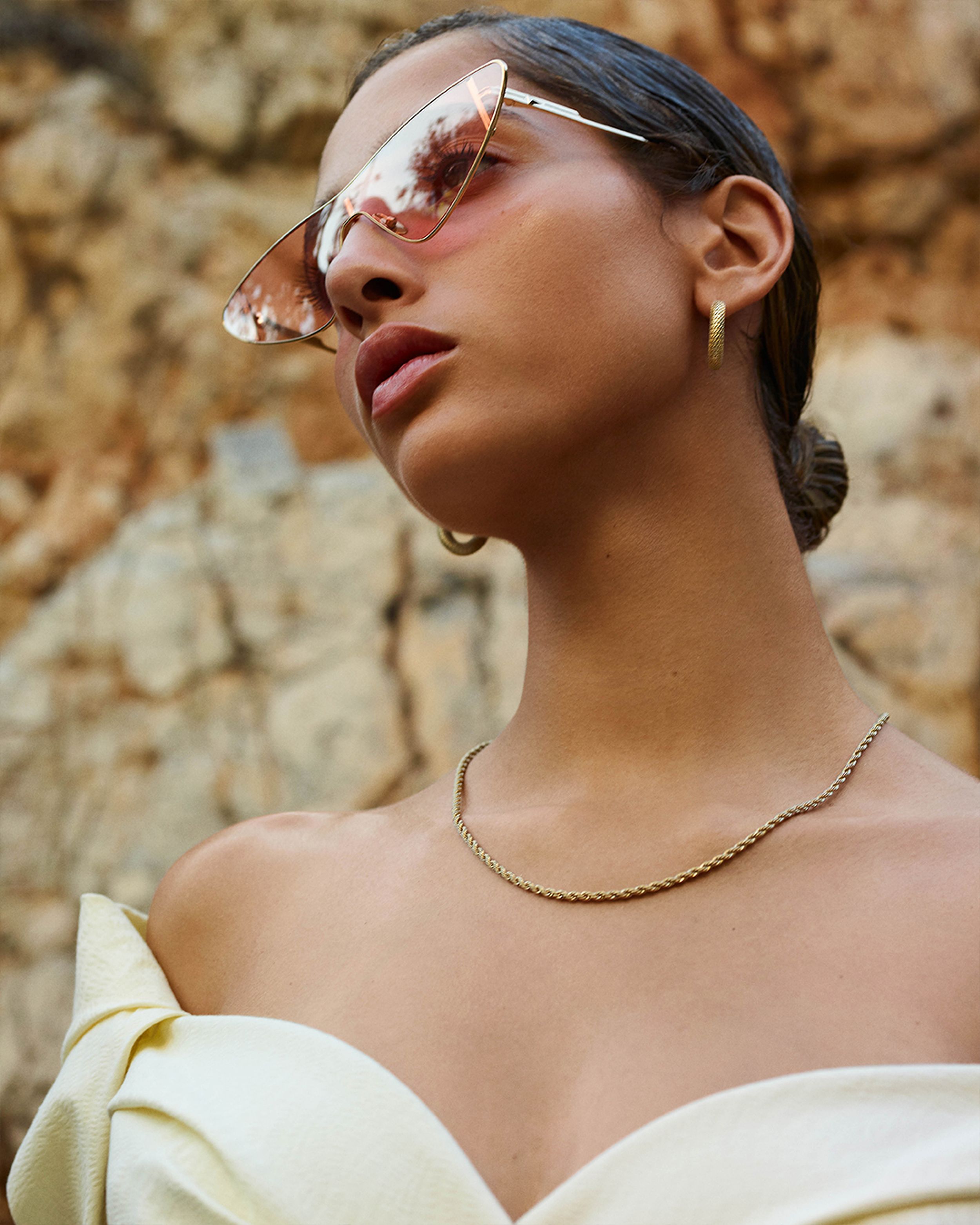 Yasmin Wijnaldum gazing to the side wearing a cream dress, sunglasses and gold chain