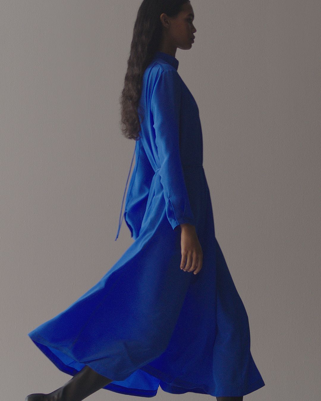 Woman walking in front of the camera on grey background in cobalt blue long sleeve dress.