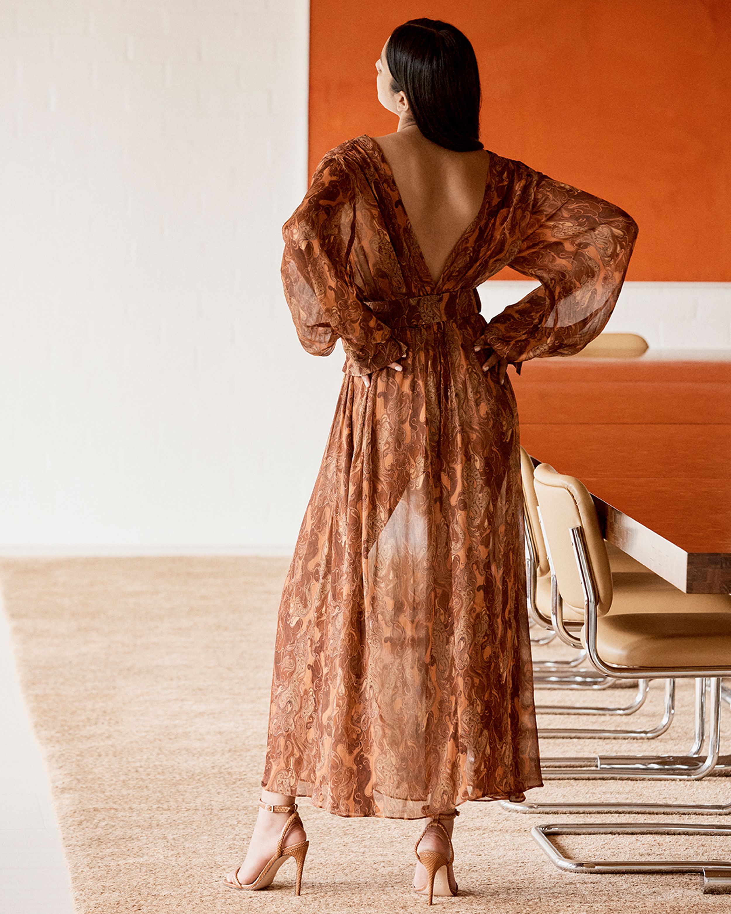 Brunette model standing facing away wearing a brown print dress