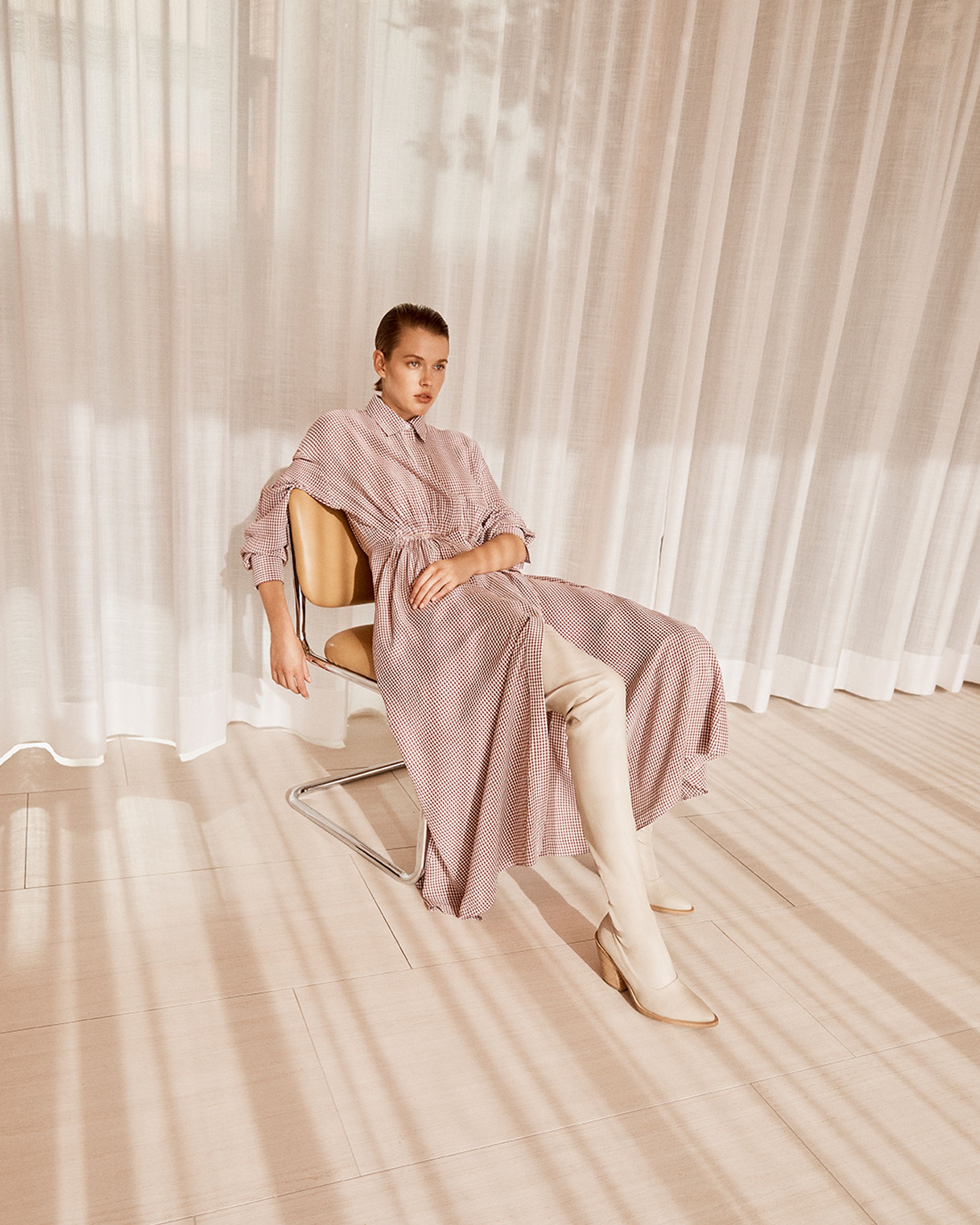 Model sitting in armchair wearing a houndstooth midi dress and white leather boots