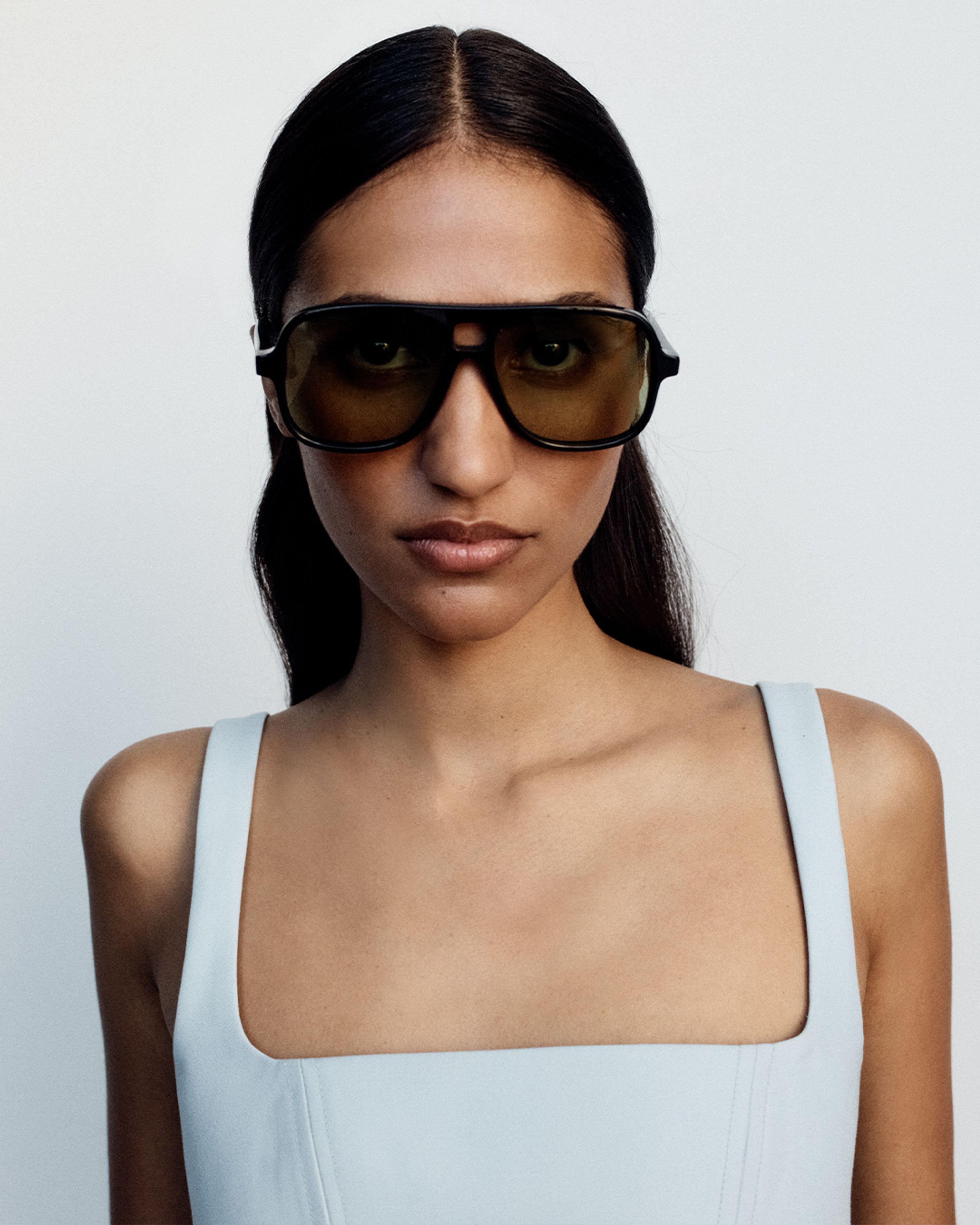 Model facing front on wearing black aviator sunglasses and a white singlet