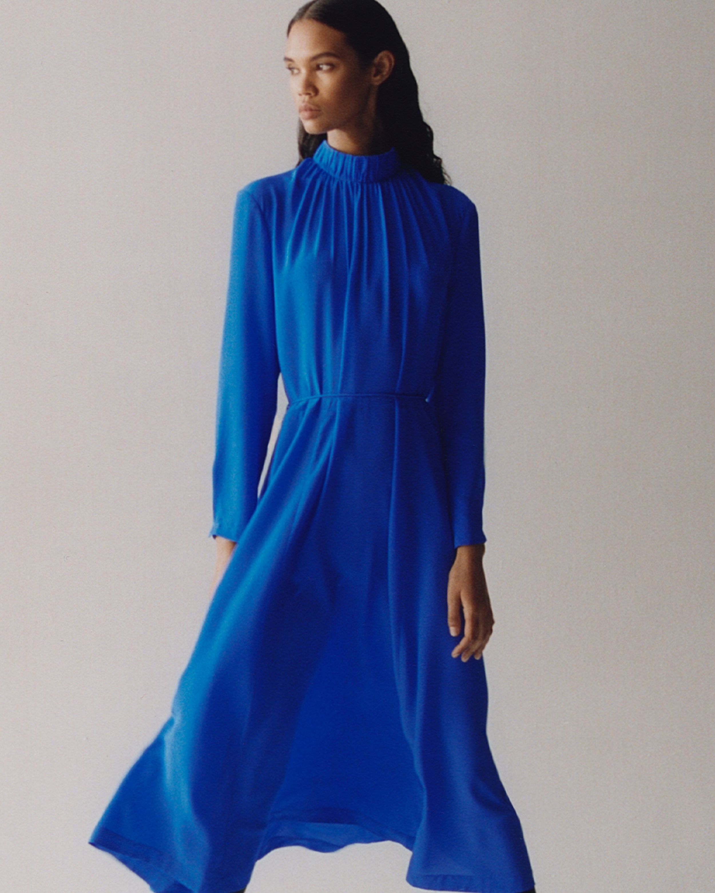 Brunette woman with curly hair looking away from camera, cobalt blue dress blowing in wind.  