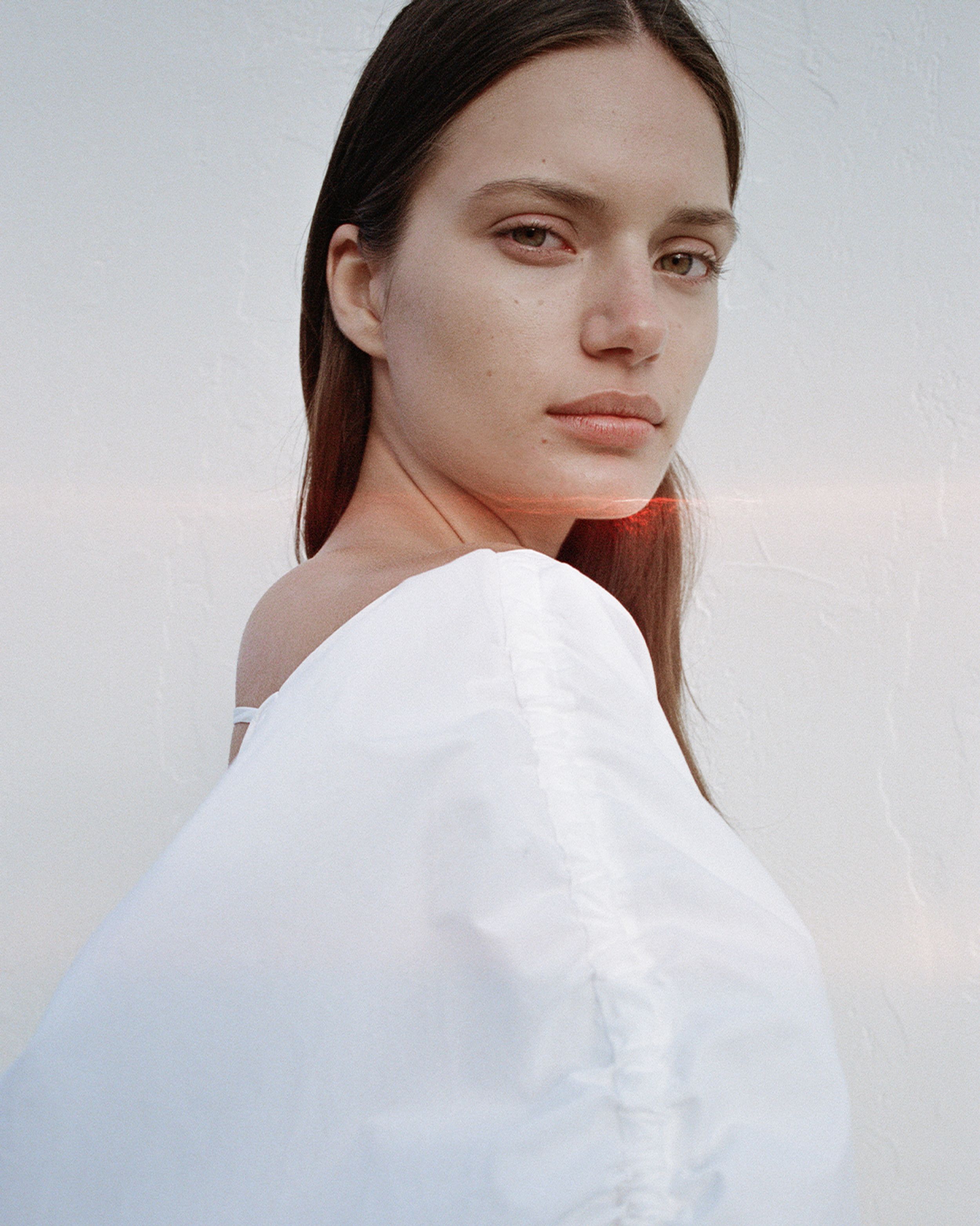 Head shot of brunette girl showing gather detail of white dress and red-light leak across her face. 