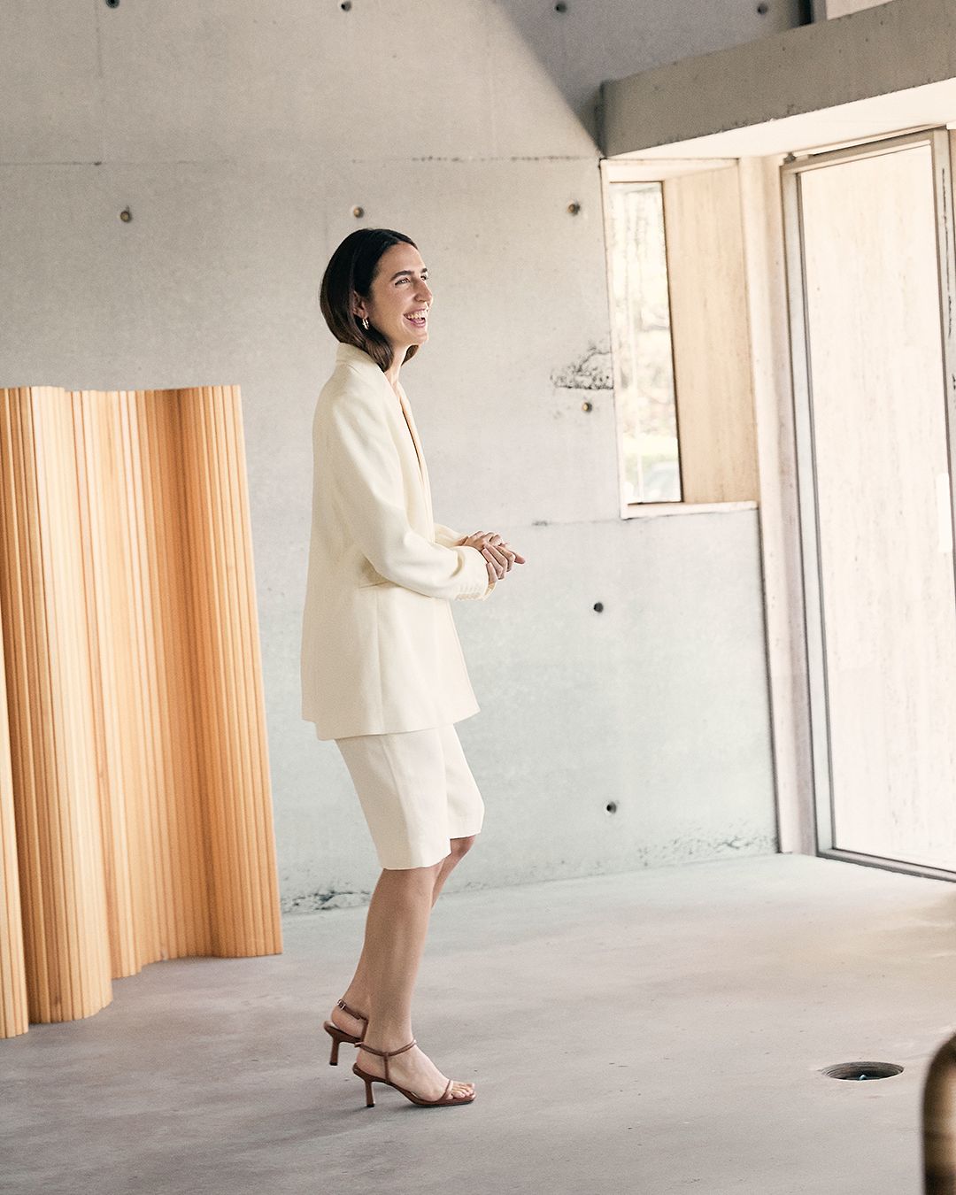 Bianca Marchi walking indoors wearing a cream oversized jacket and cream shorts