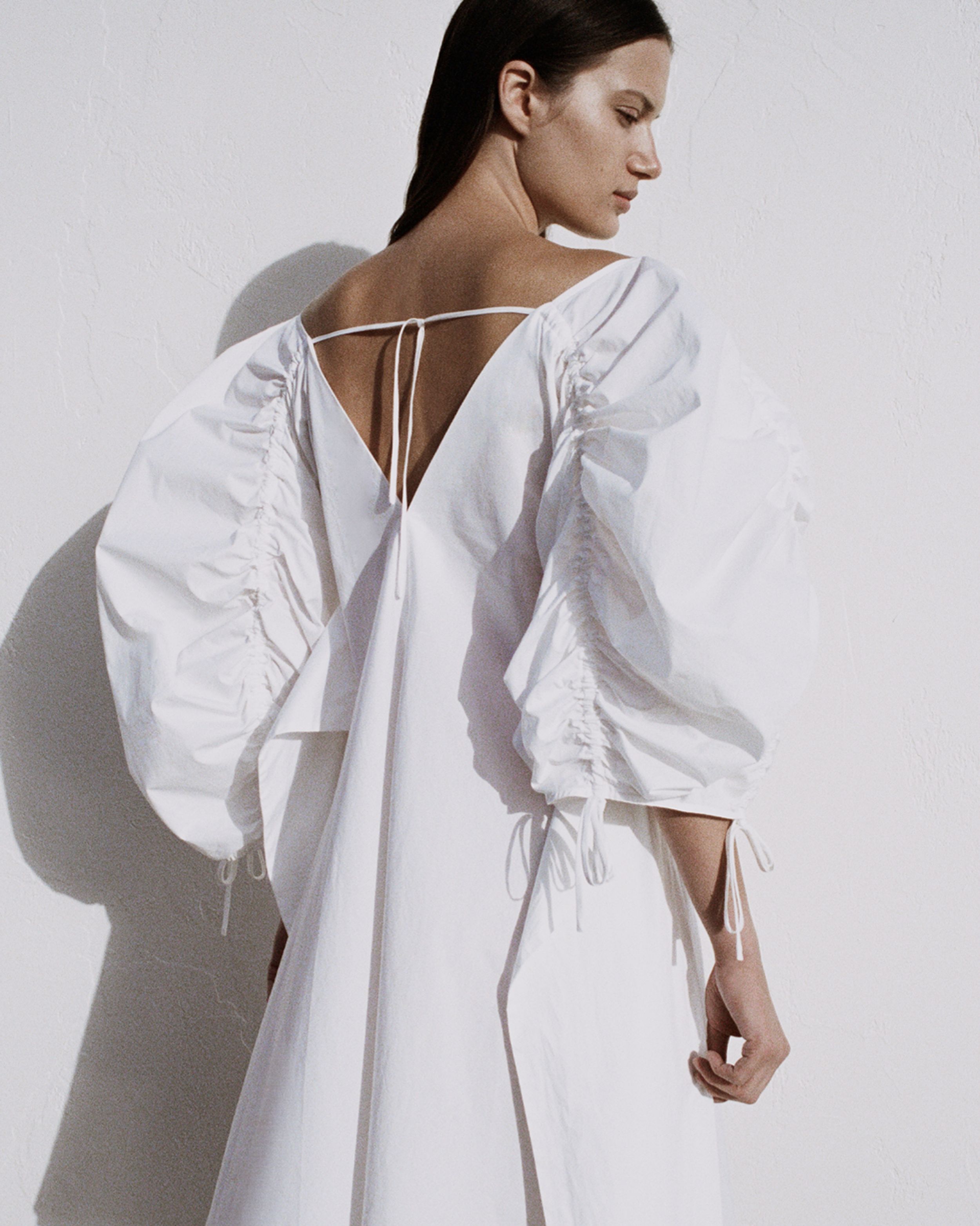 Girl facing away from the camera looking over her shoulder in a white dress and shadow on the wall. 