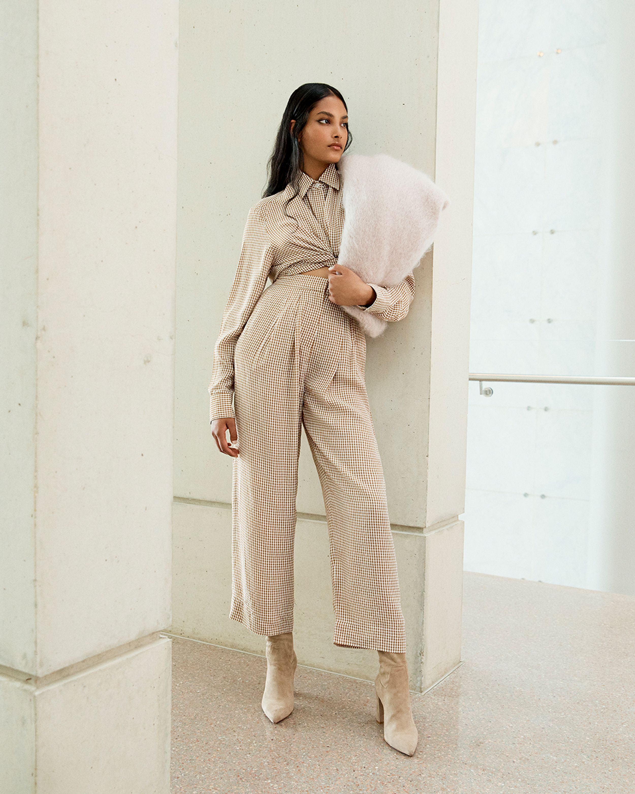 Model leaning against a wall wearing a matching checked shirt and trousers with scarf over her shoulder