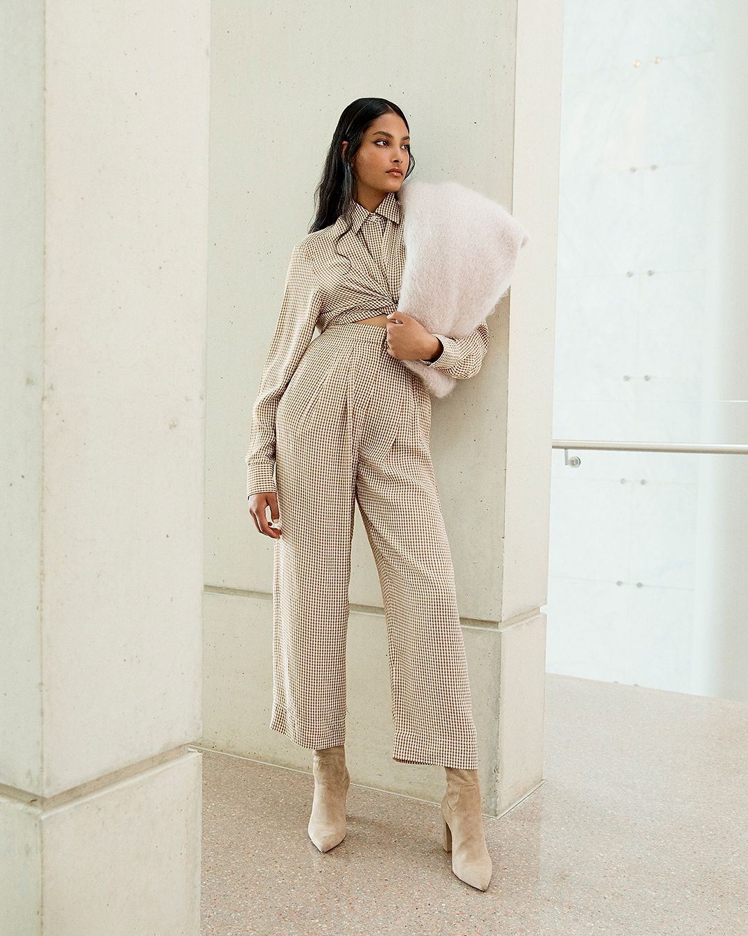 Model leaning against a wall wearing a matching checked shirt and trousers with scarf over her shoulder