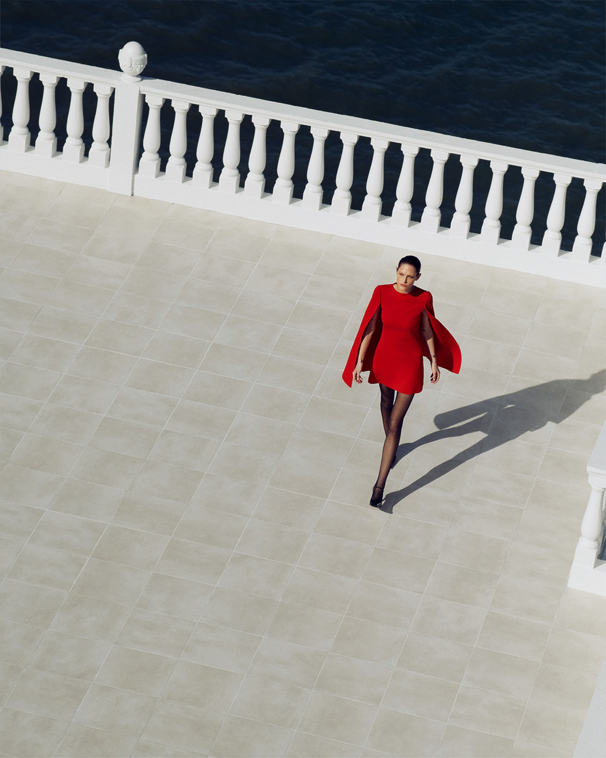 Arial view of model in Crepe Knit Red Cape Dress walking on tiled balcony