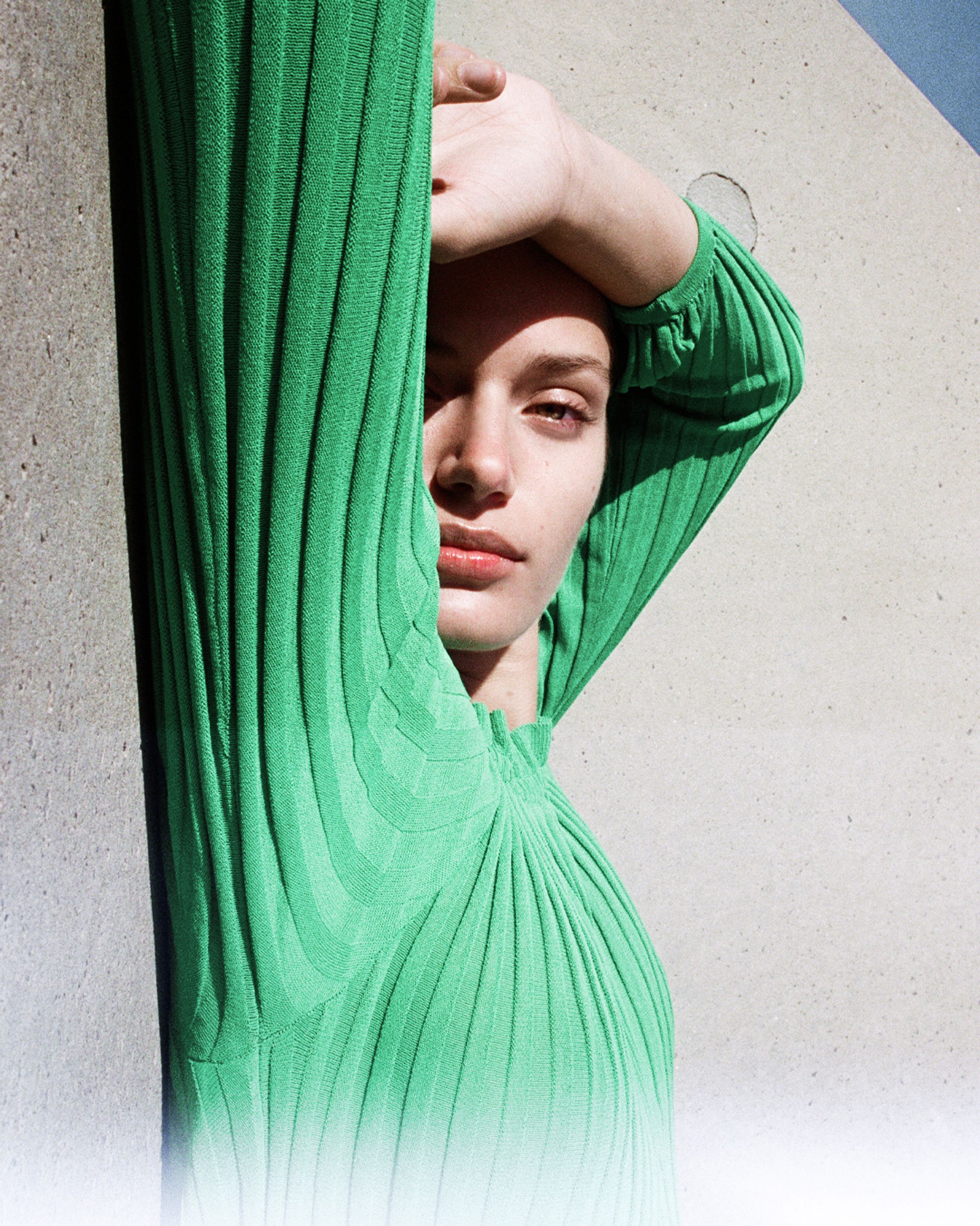 Head shot of brunette girl with shadow coming across her face, one eye squinting from the sun. 